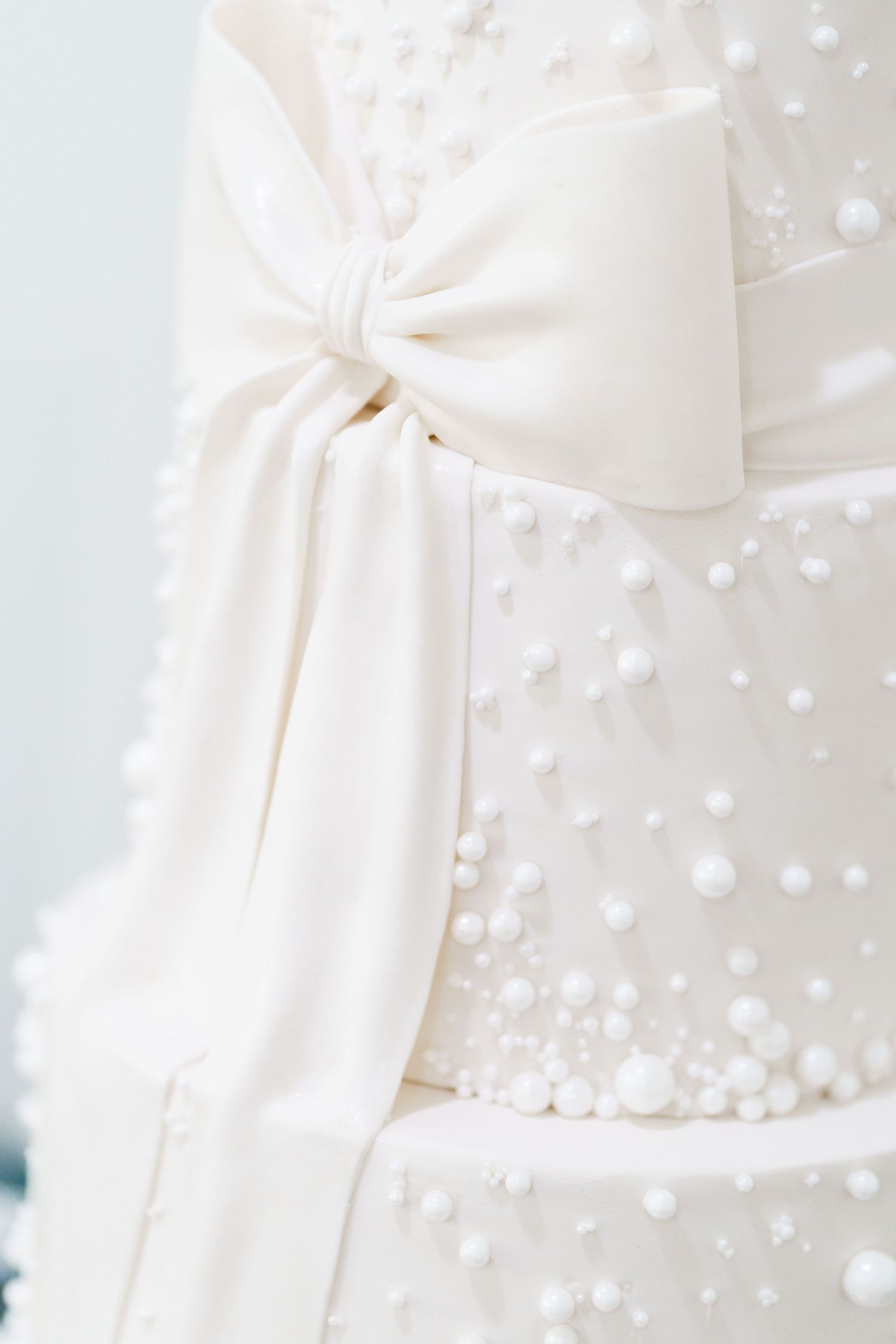 Close up detail of a white wedding cake with delicate polka dot details and an elegant bow decoration.