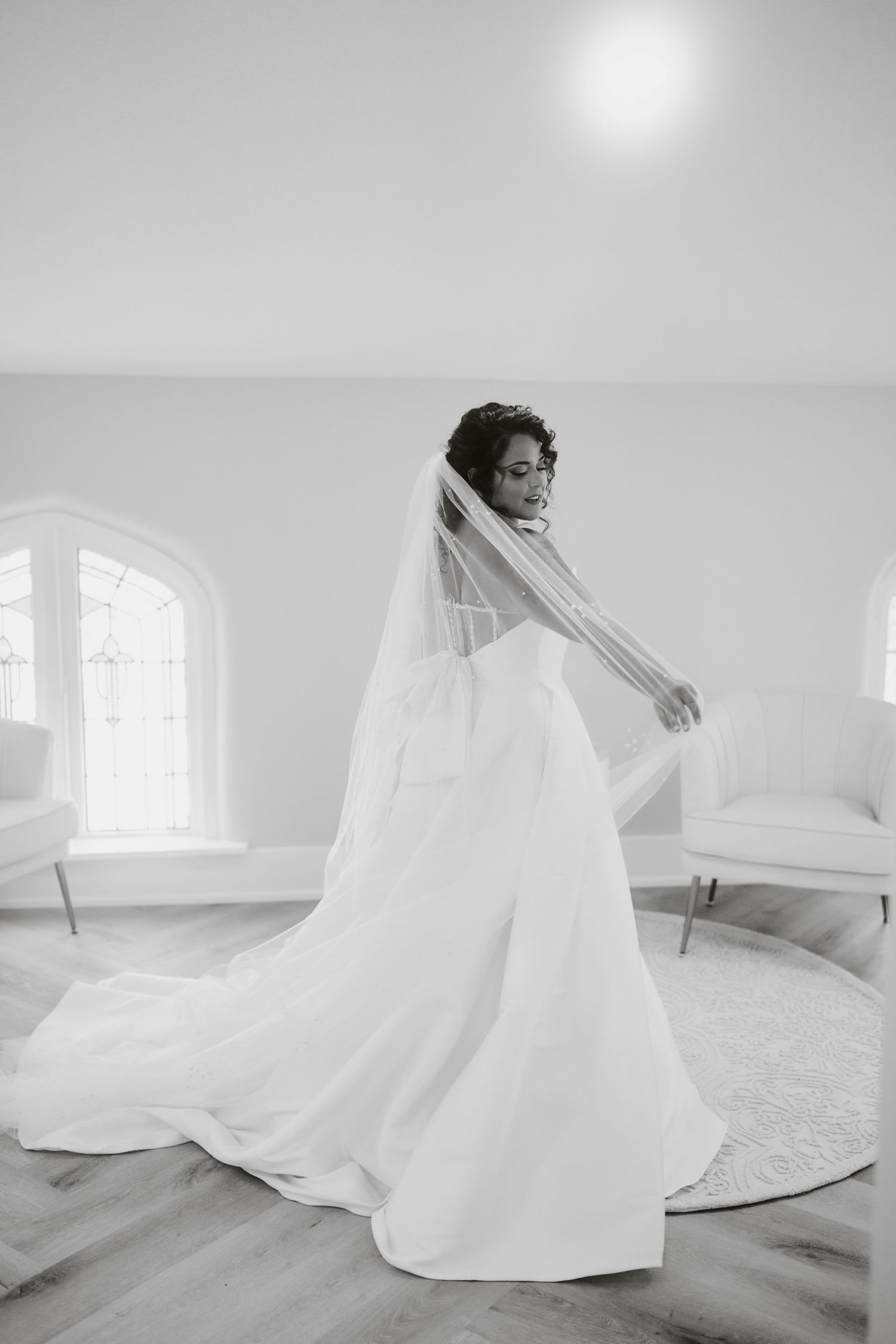 A bride in a flowing white gown and veil twirls elegantly in a bright, minimalist room.