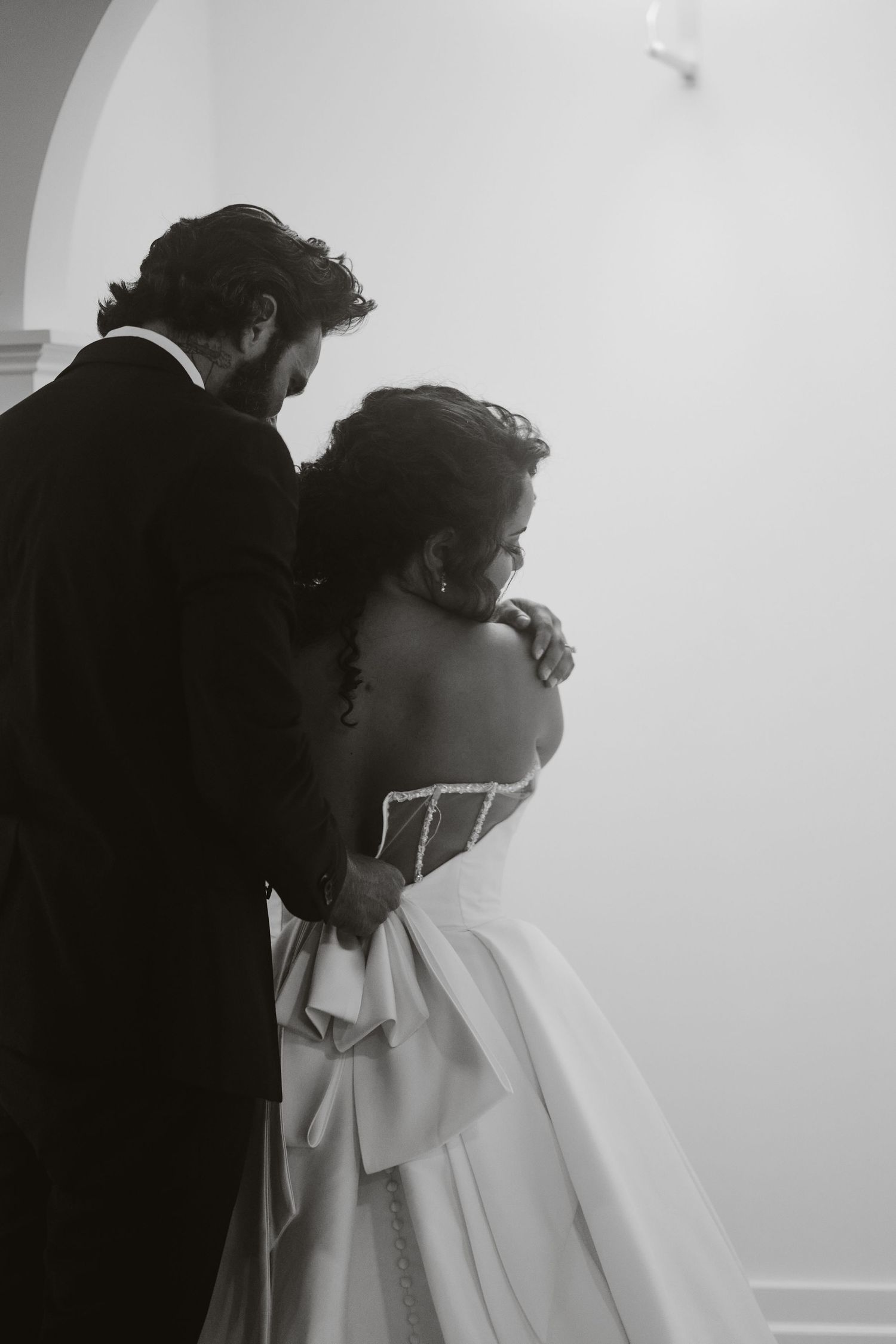 Black and white photo capturing an intimate moment between a couple in formal wedding attire.