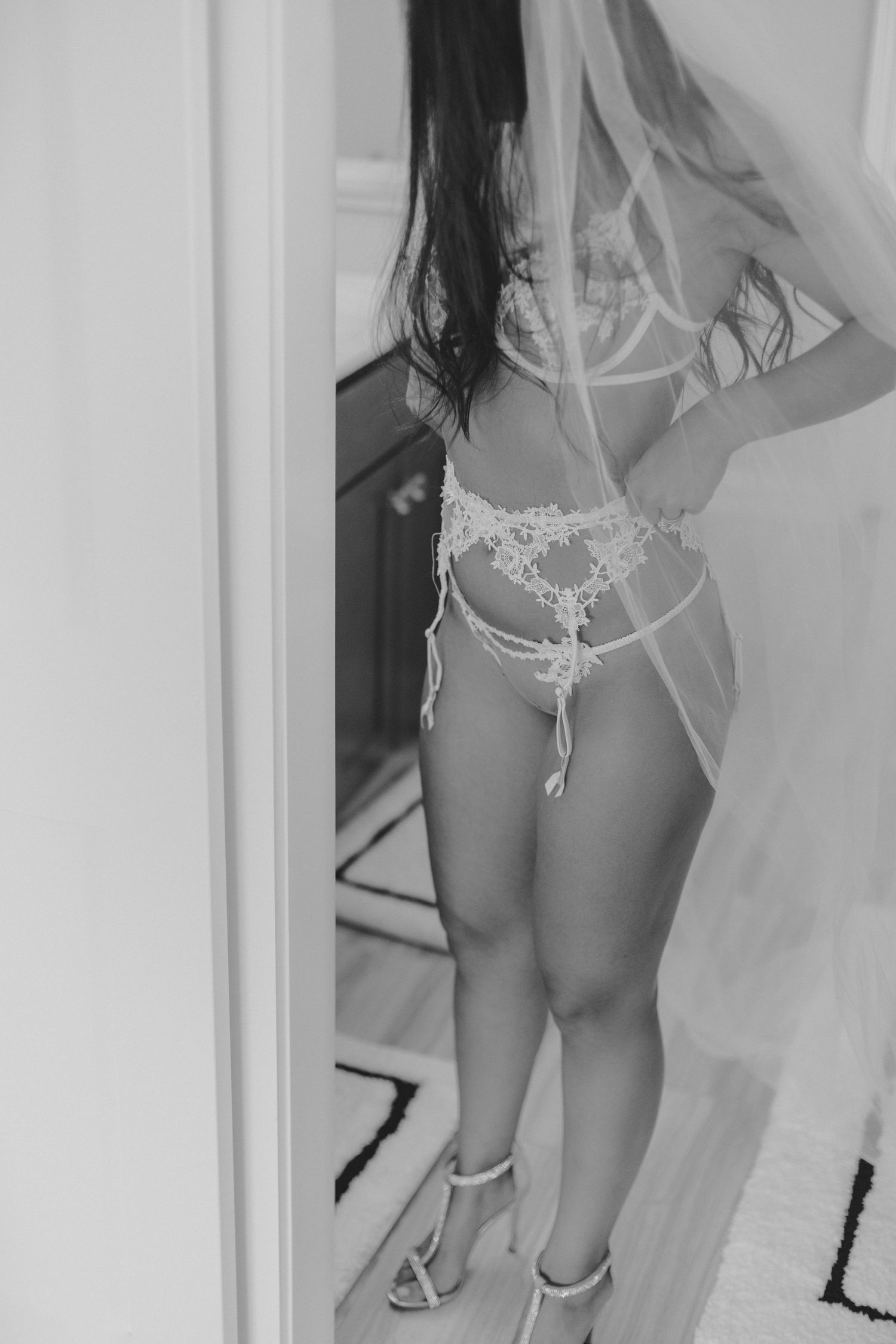 Black and white image showing legs in white high heels and lacy bridal lingerie with sheer fabric flowing in background.