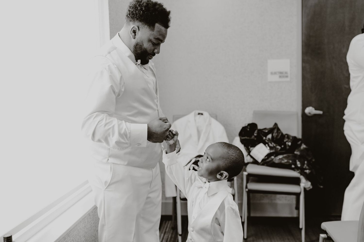 Black and white photo of a touching moment between a child and adult in white formal wear.
