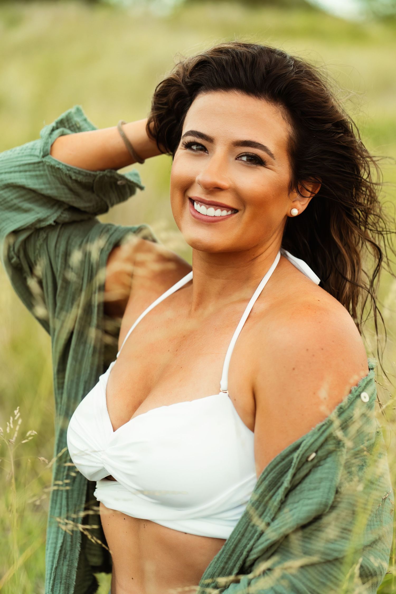 Woman in white swimwear and green jacket poses outdoors with natural smile.
