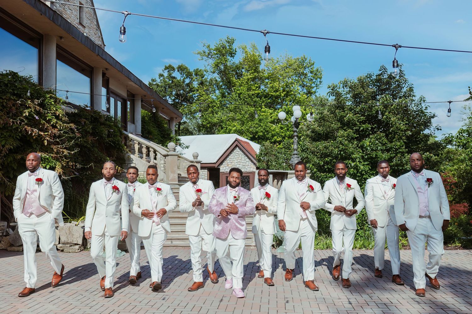 Wedding party in white suits walking together on outdoor patio during summer celebration.