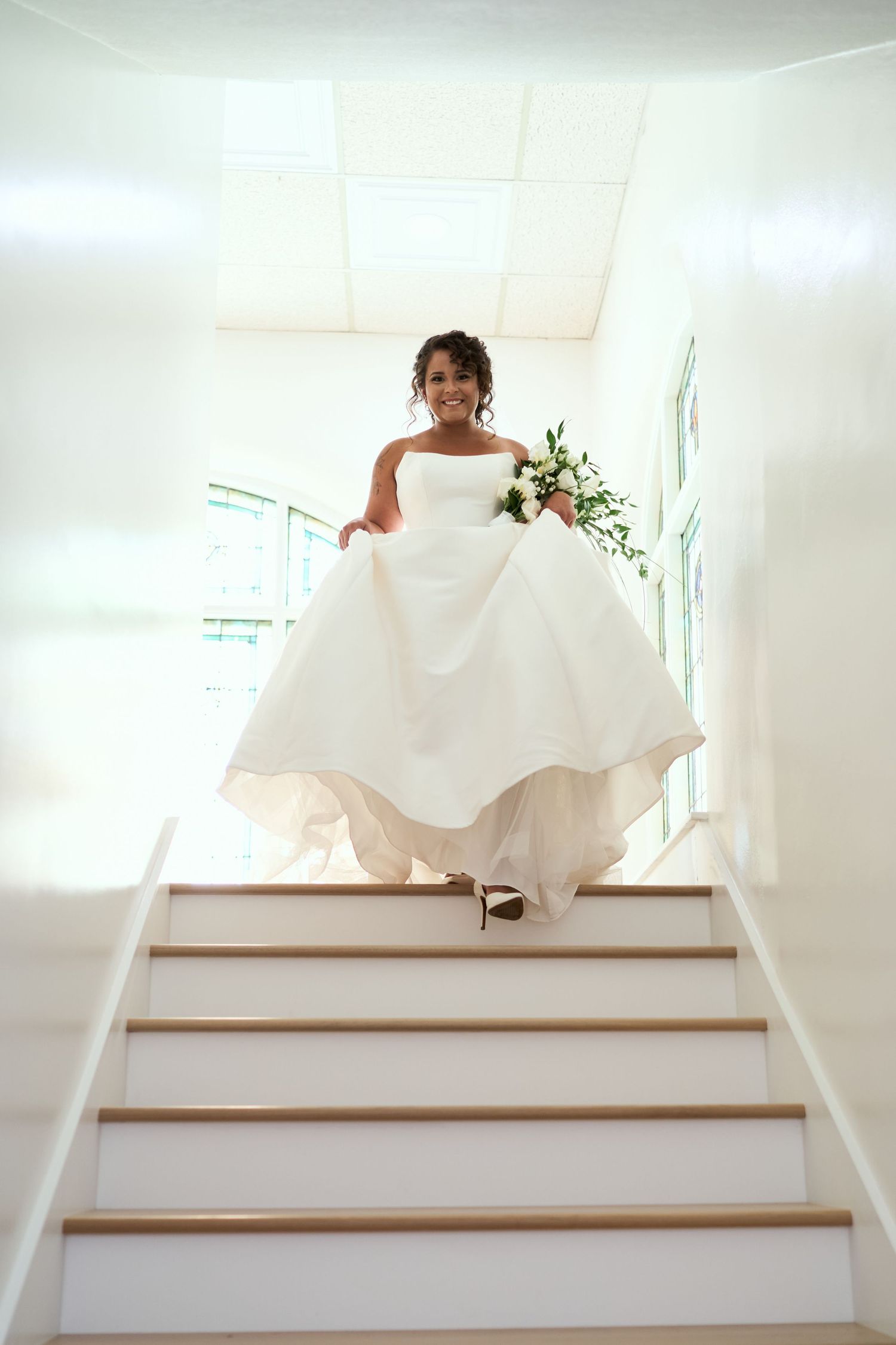 A joyful moment captured as person in white wedding gown descends staircase holding bouquet.