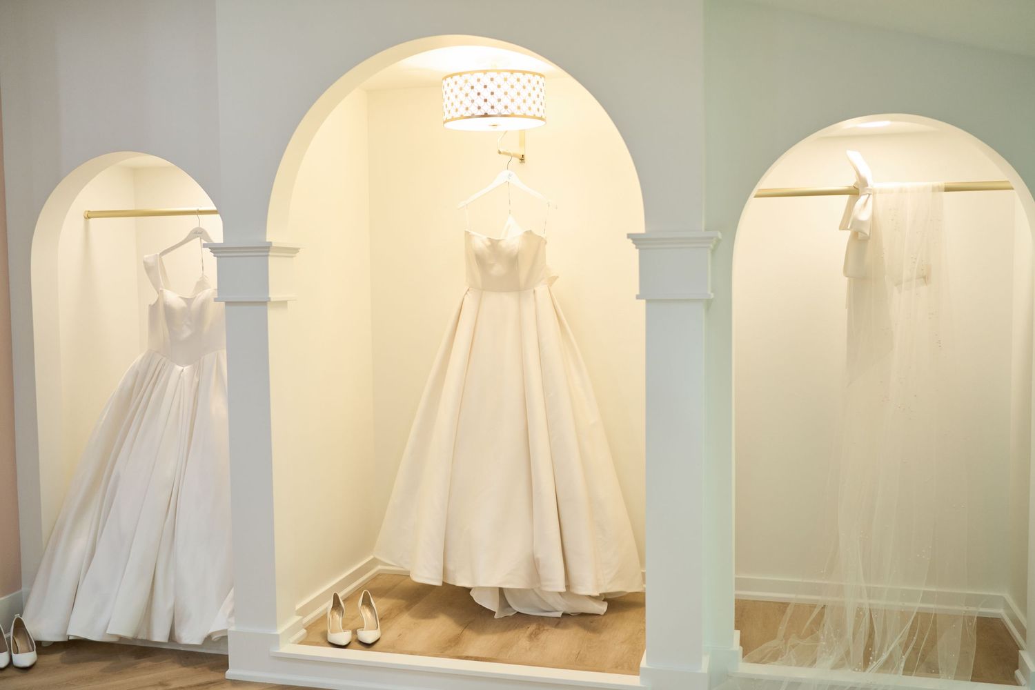 Elegant white wedding dresses displayed in illuminated arched alcoves at a bridal boutique store.