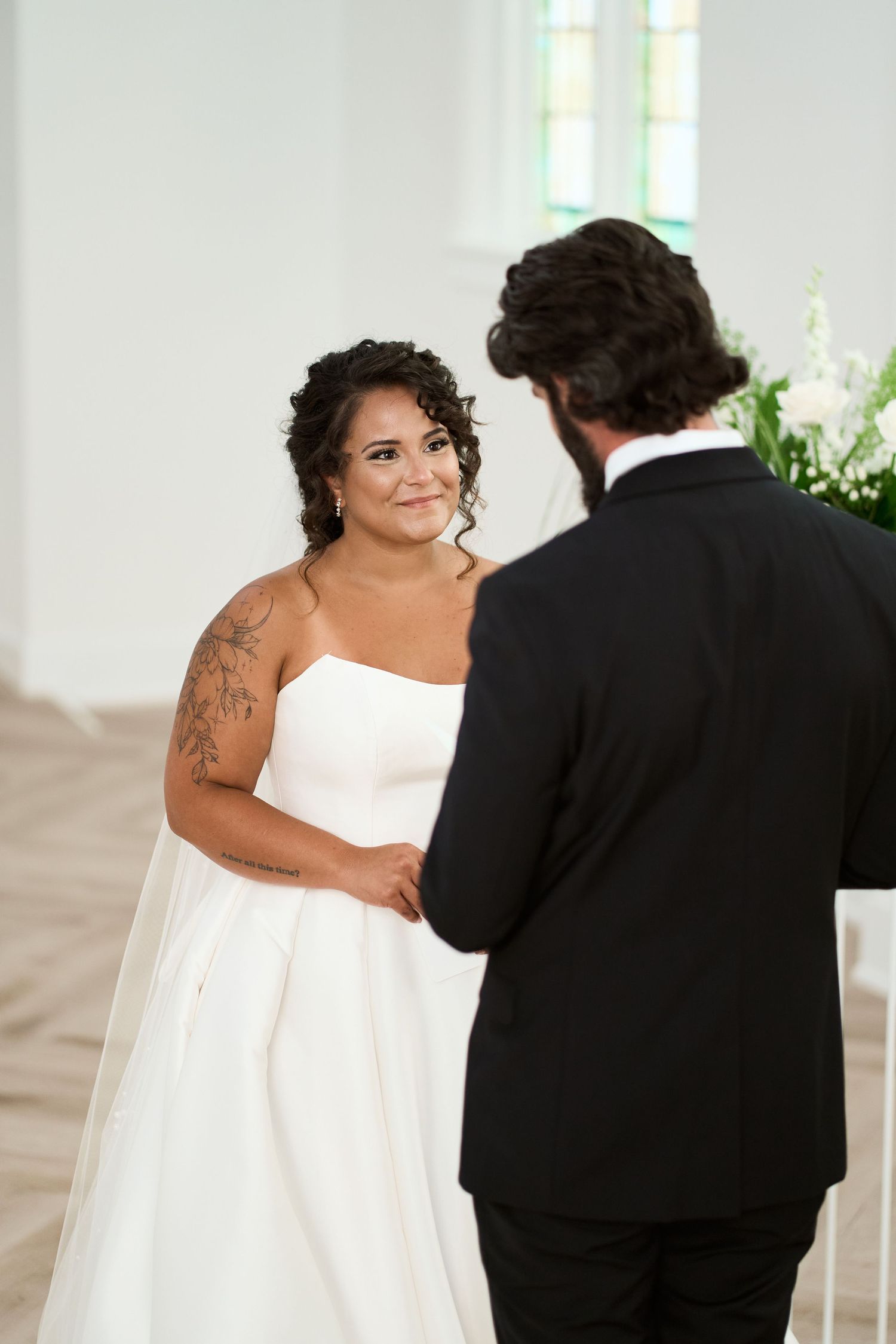 An intimate wedding ceremony exchange in a bright church setting with stained glass windows.