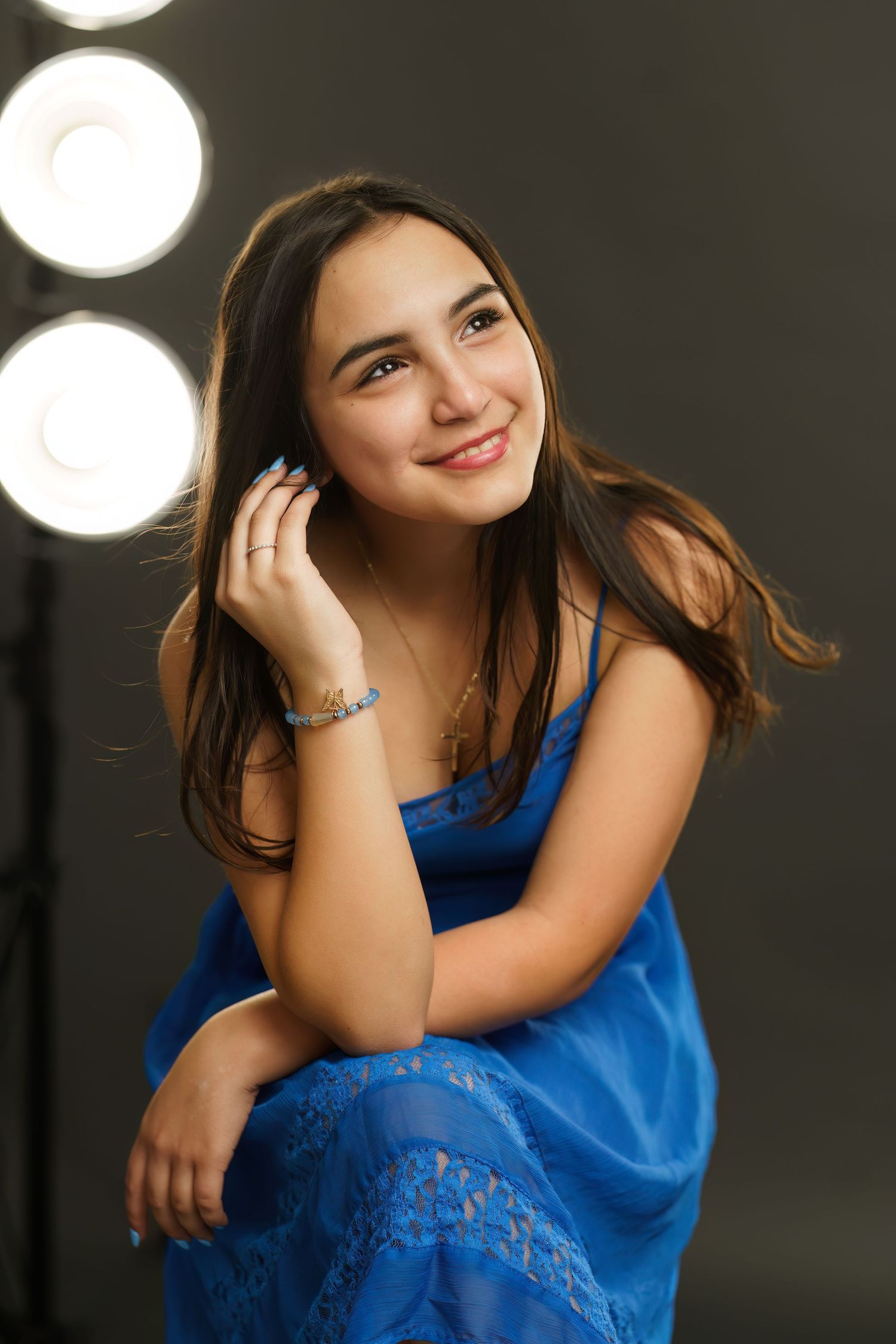 Portrait of a young woman in a bright blue dress smiling warmly against a dark background with bokeh lights.