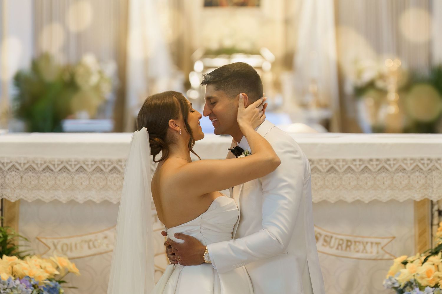 A couple shares a romantic moment during their wedding ceremony surrounded by elegant floral decorations and white decor.