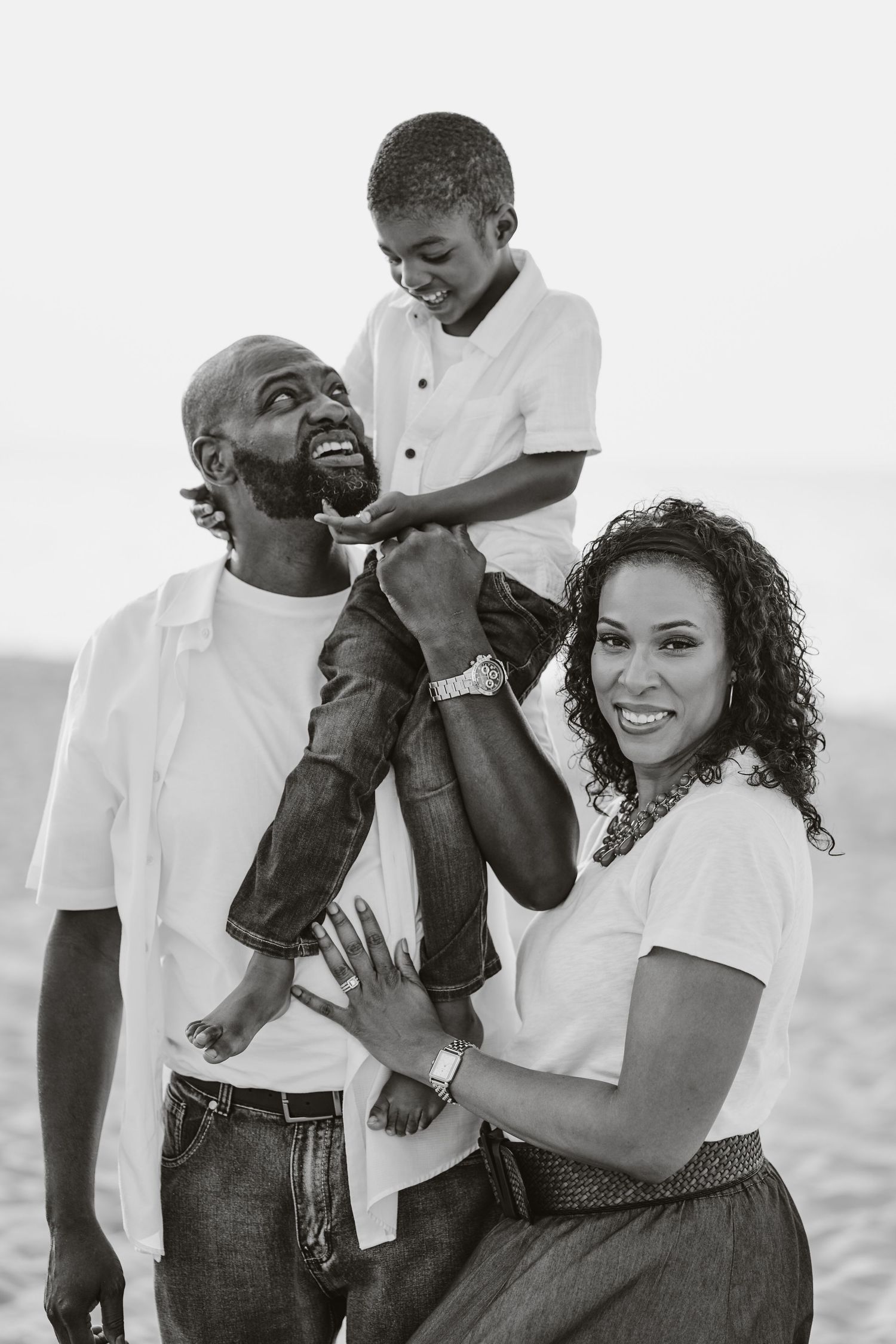 A joyful family shares a candid black and white moment together at the beach.