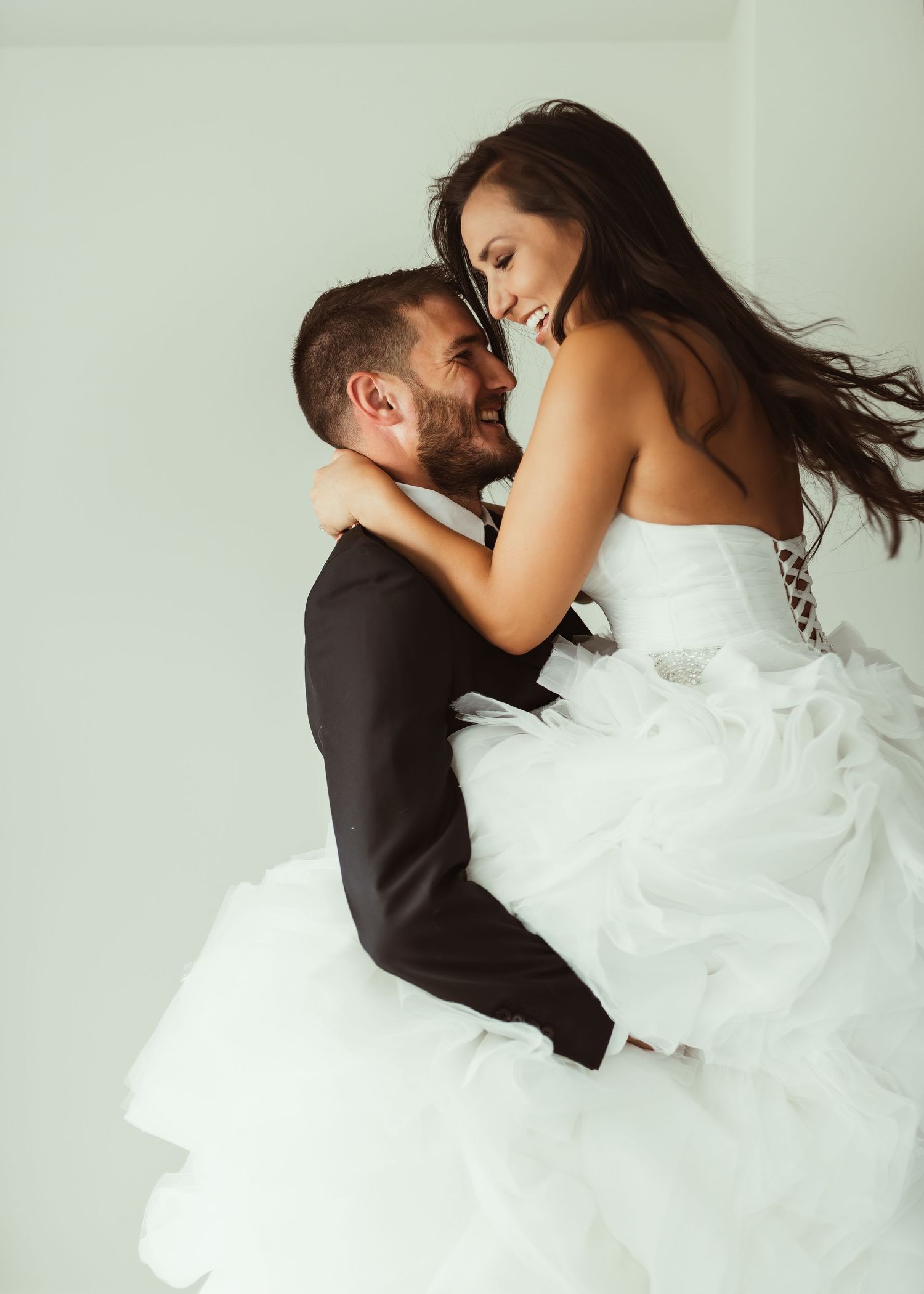 Romantic wedding portrait showing joyful couple in black suit and white gown.