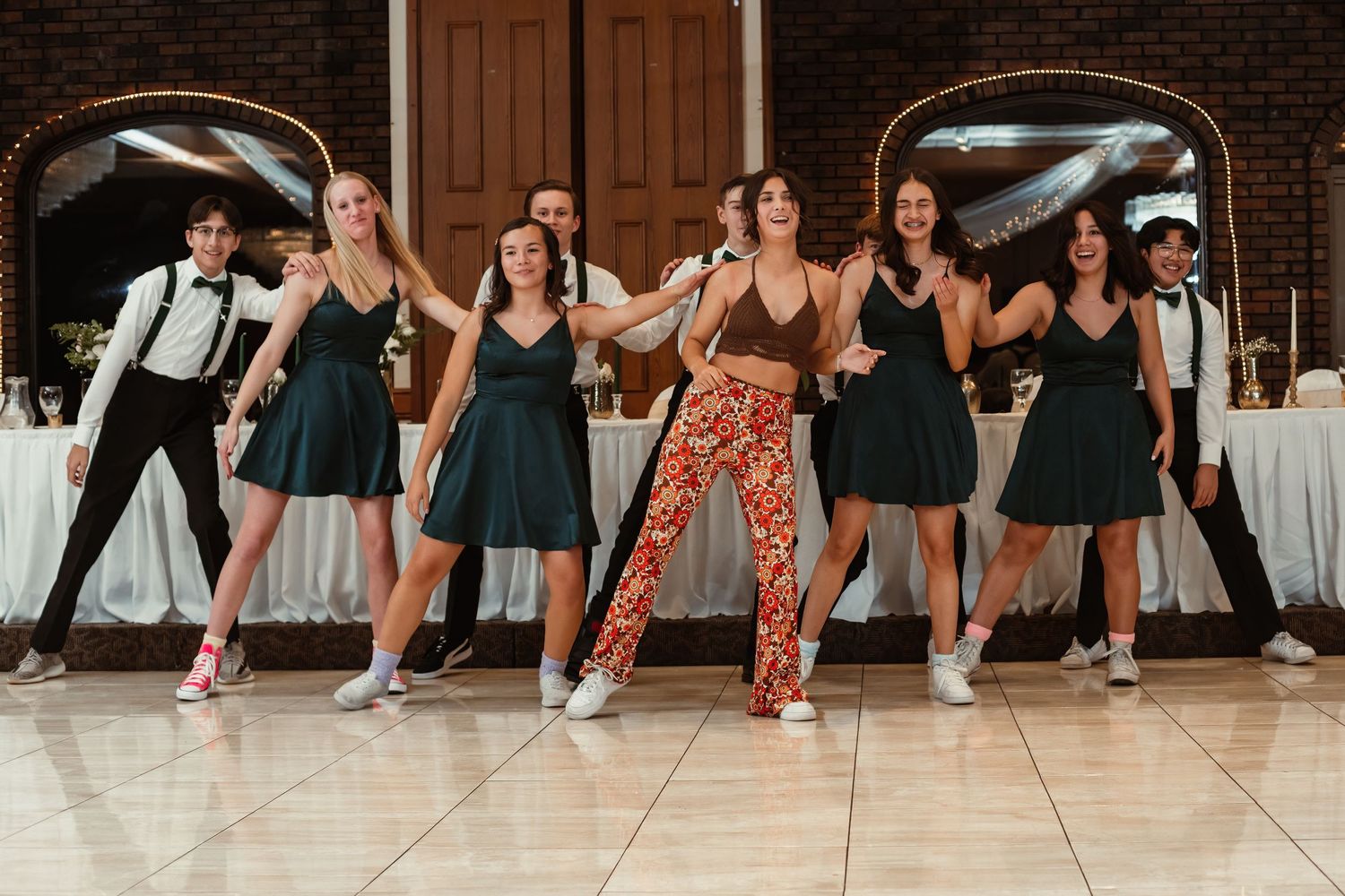 Wedding guests dance in a line wearing black dresses and formal attire at a reception.