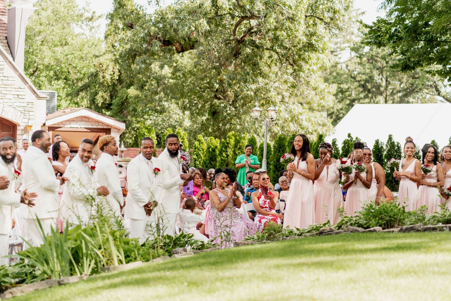 Wedding guests in white and pink attire gathered outdoors for a garden ceremony.