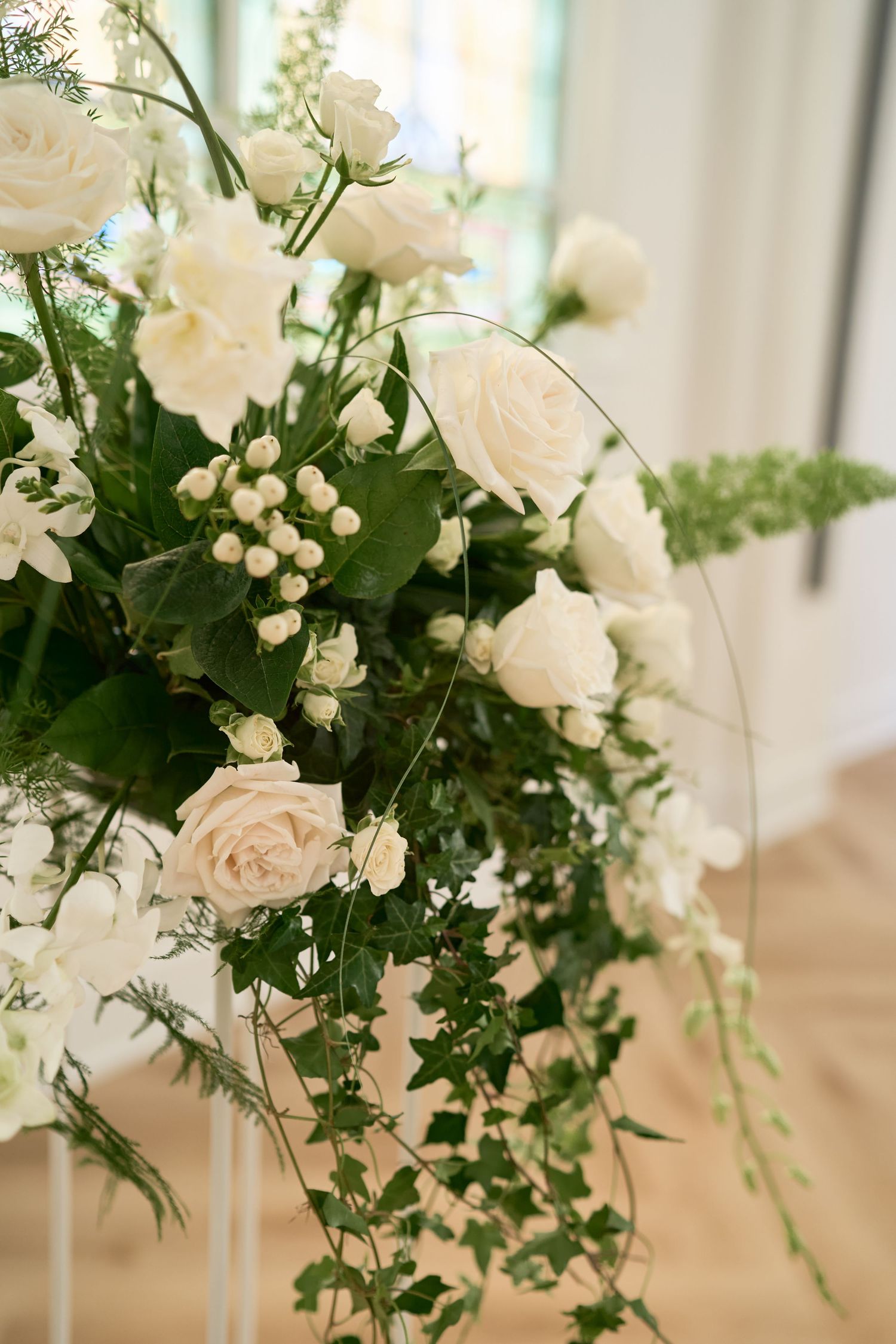 Elegant white rose and greenery floral arrangement in a soft, light-filled setting.