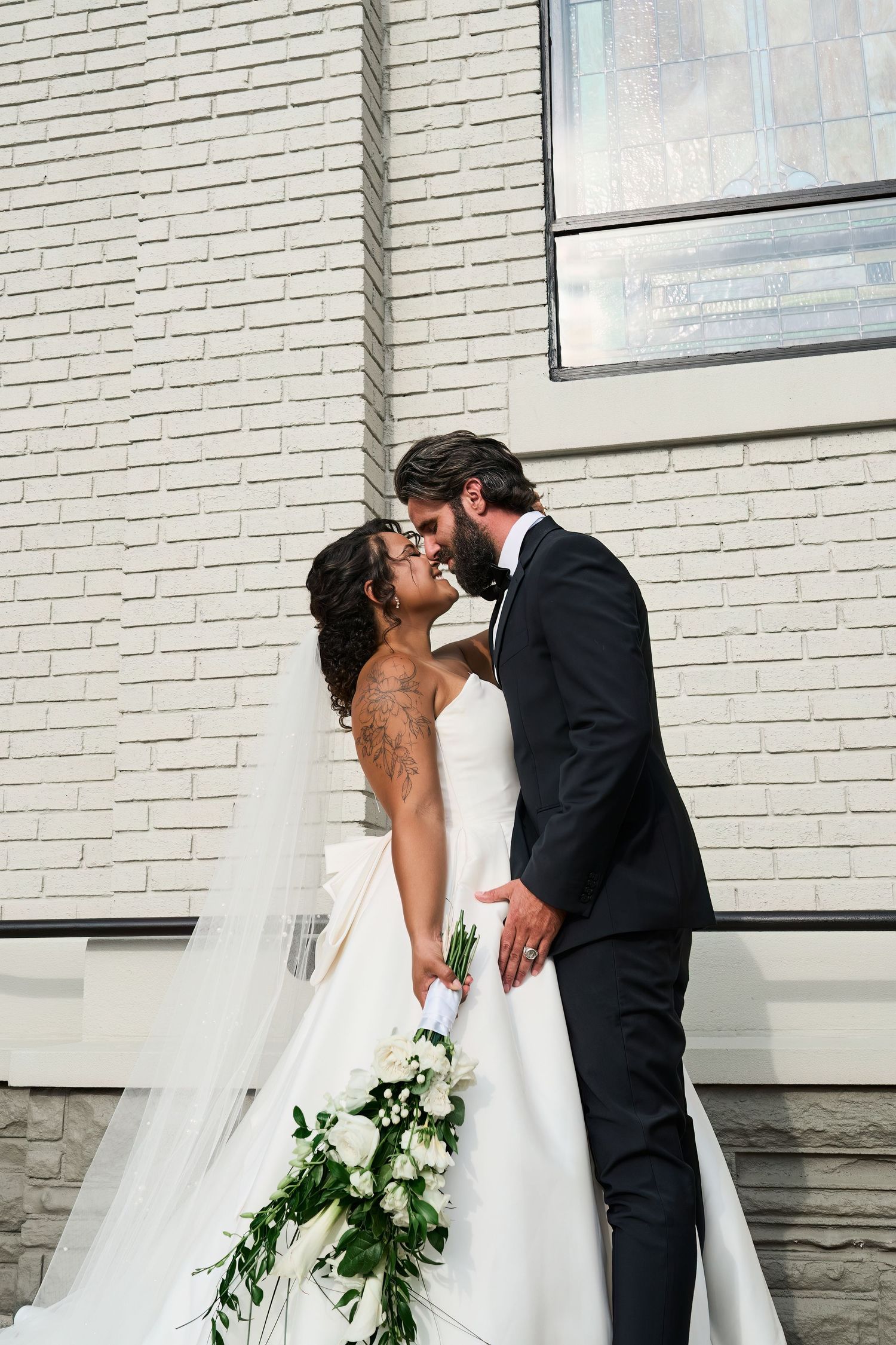 A romantic wedding photo showing a couple kissing while the bride holds a cascading white bouquet at Kaleidoscope  venue in Pierceton,  IN