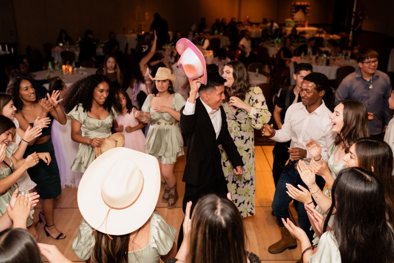 Wedding guests dancing and celebrating together on a crowded dance floor at an indoor reception venue.