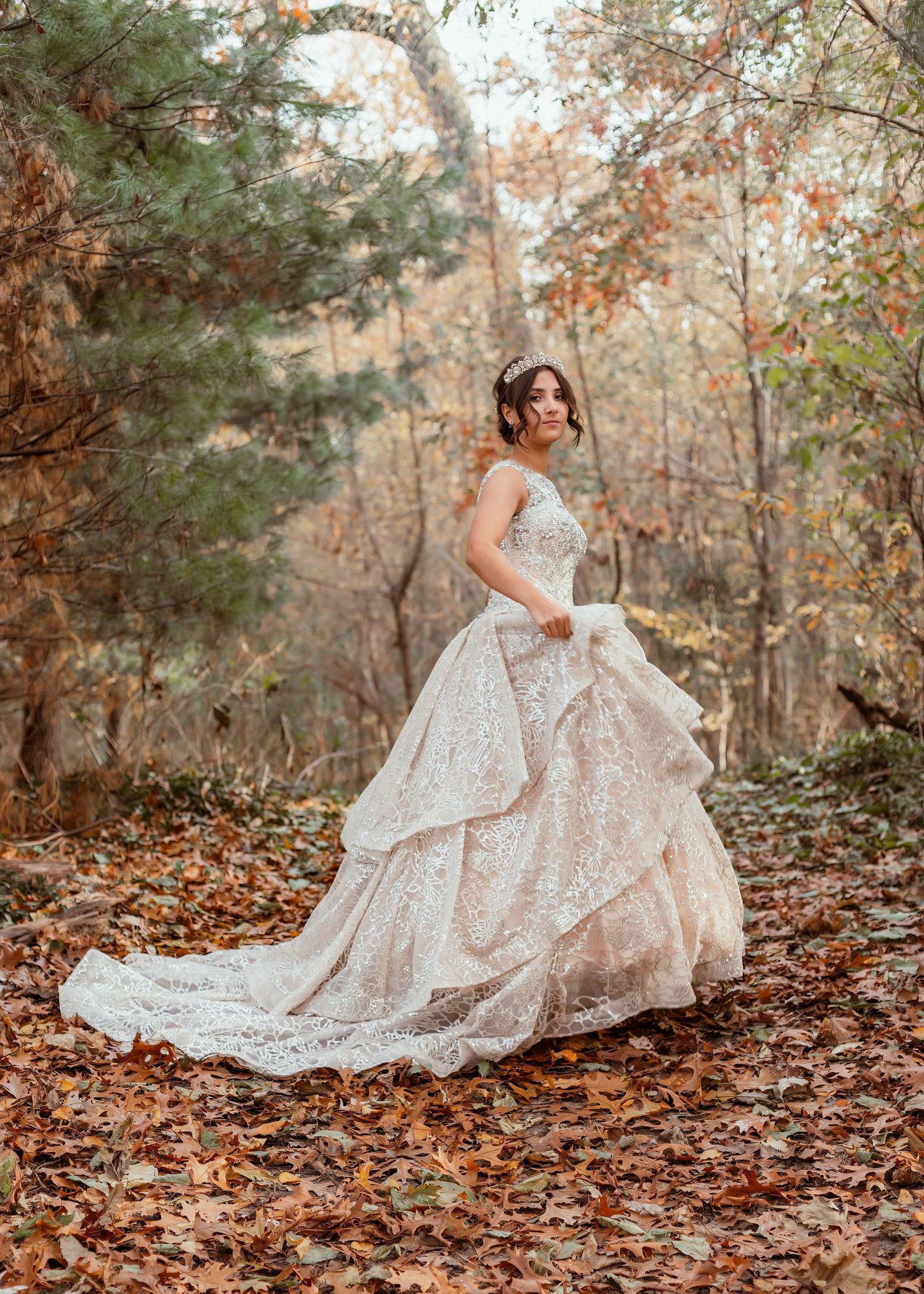 Lace ball gown with layered skirt photographed in autumn forest setting with fallen leaves.