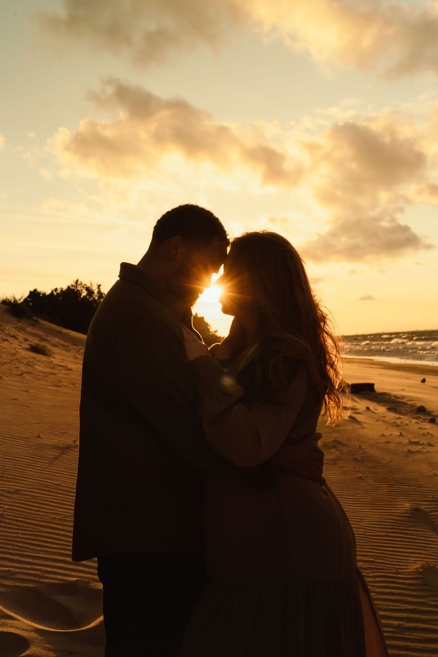 Backlit silhouette of couple in tender moment during golden hour on sand dunes.
