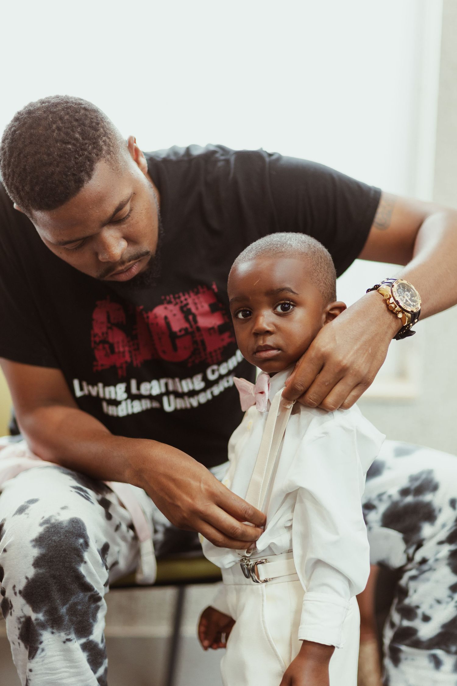 Adult helping young child get dressed in white outfit.