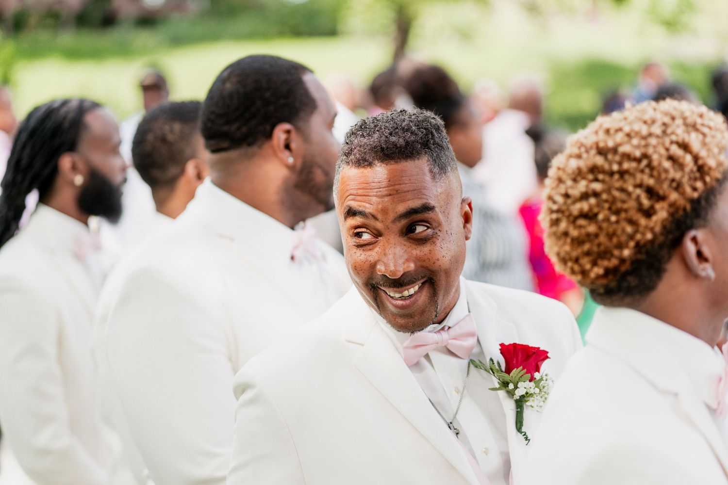 Wedding party members in white suits share a joyful moment outdoors.