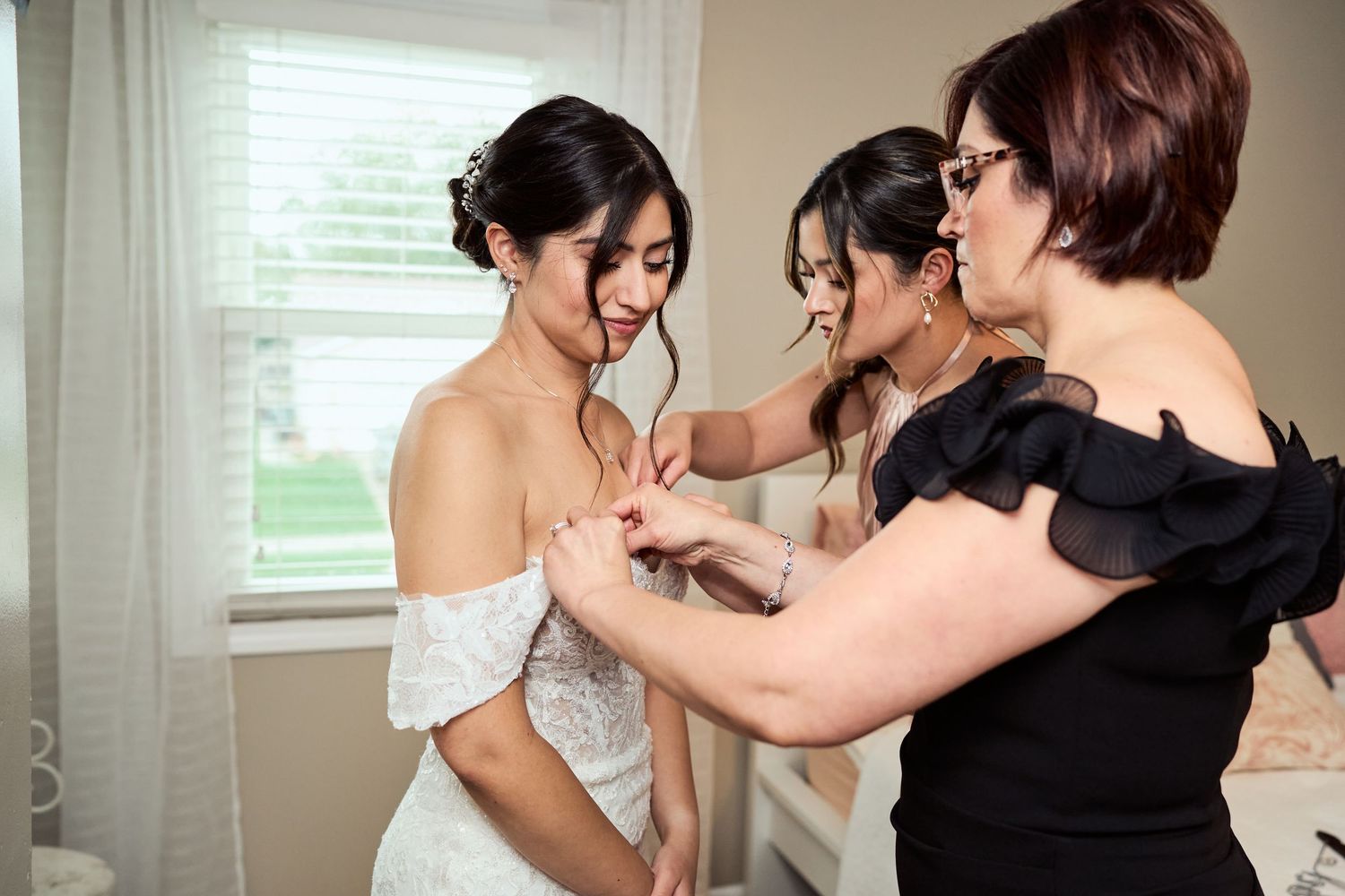 A bride getting ready with her bridesmaids in black dresses helping with final preparations before the ceremony.