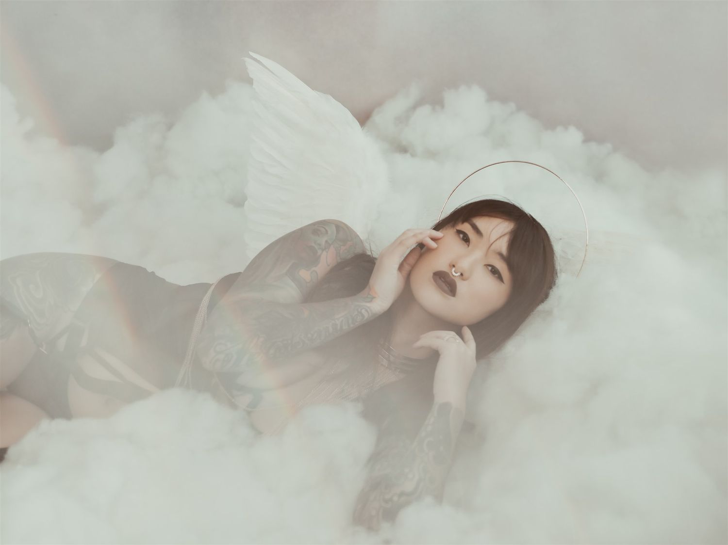 A dreamy portrait of someone laying down against a soft white cloudy background with ethereal lighting.