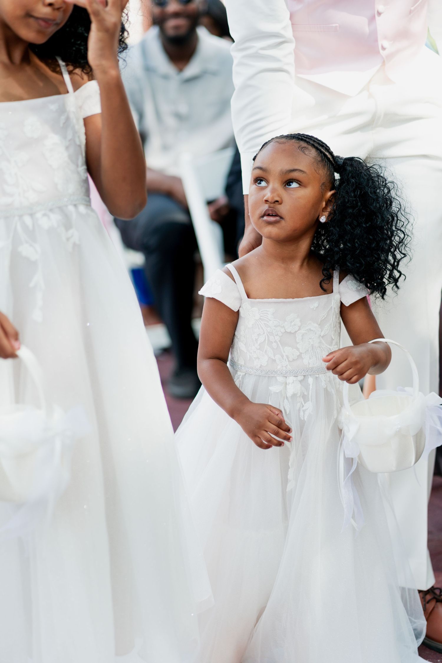 Two children wearing white dresses and curly hairstyles during a formal event.