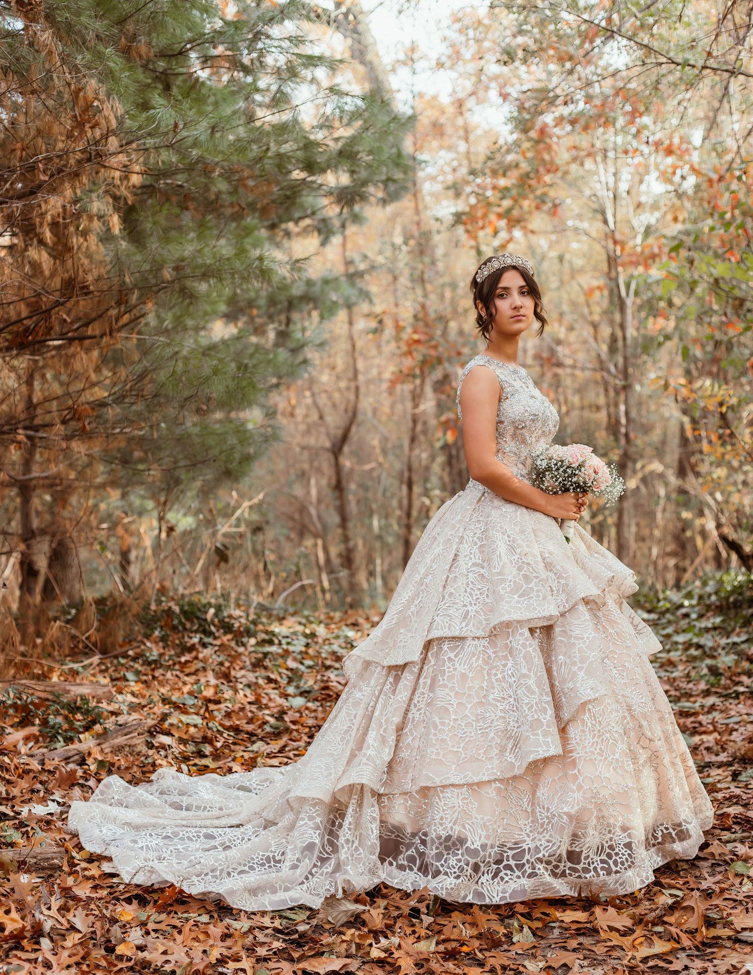 Dramatic full-length shot of a tiered lace wedding dress amid fall leaves and pine trees.