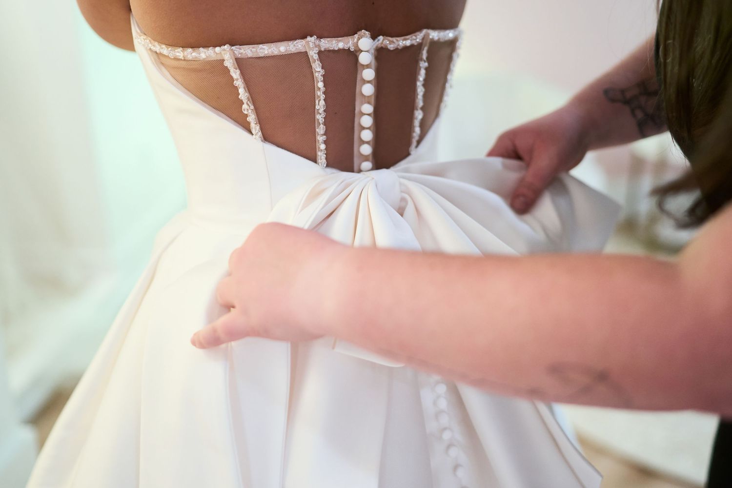 Close-up details of wedding dress buttons and fasteners being secured.