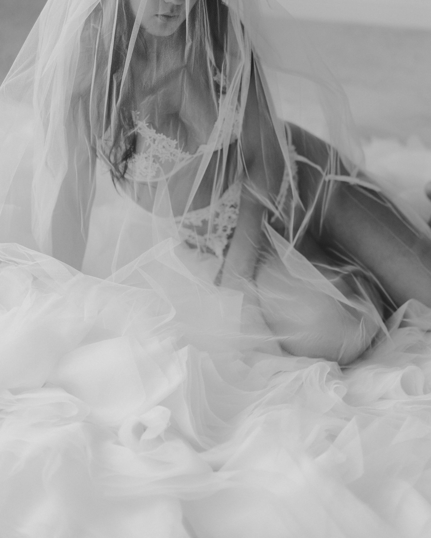 Dreamy black and white bridal boudoir photo with flowing veil and lace details.
