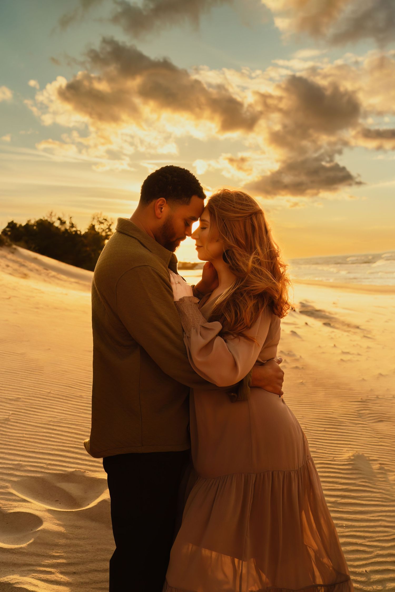 Romantic couple embracing on a beach at sunset with golden clouds in the background.