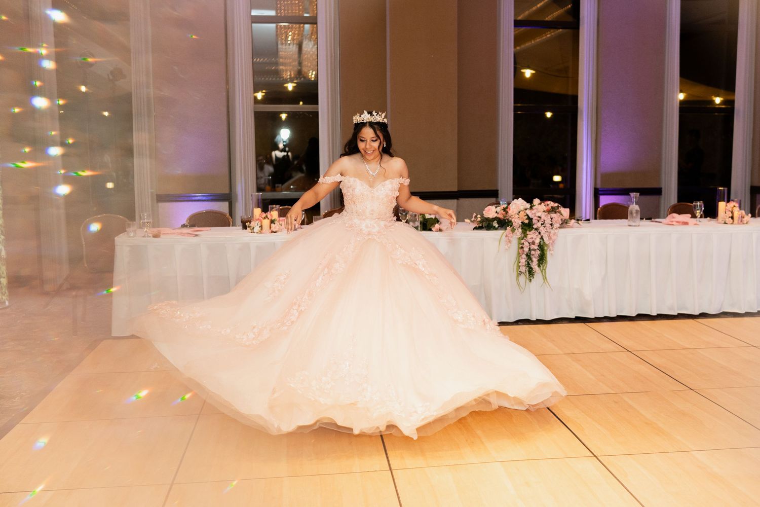 A bride in a flowing white ballgown twirls gracefully on a dance floor at an elegant wedding reception.