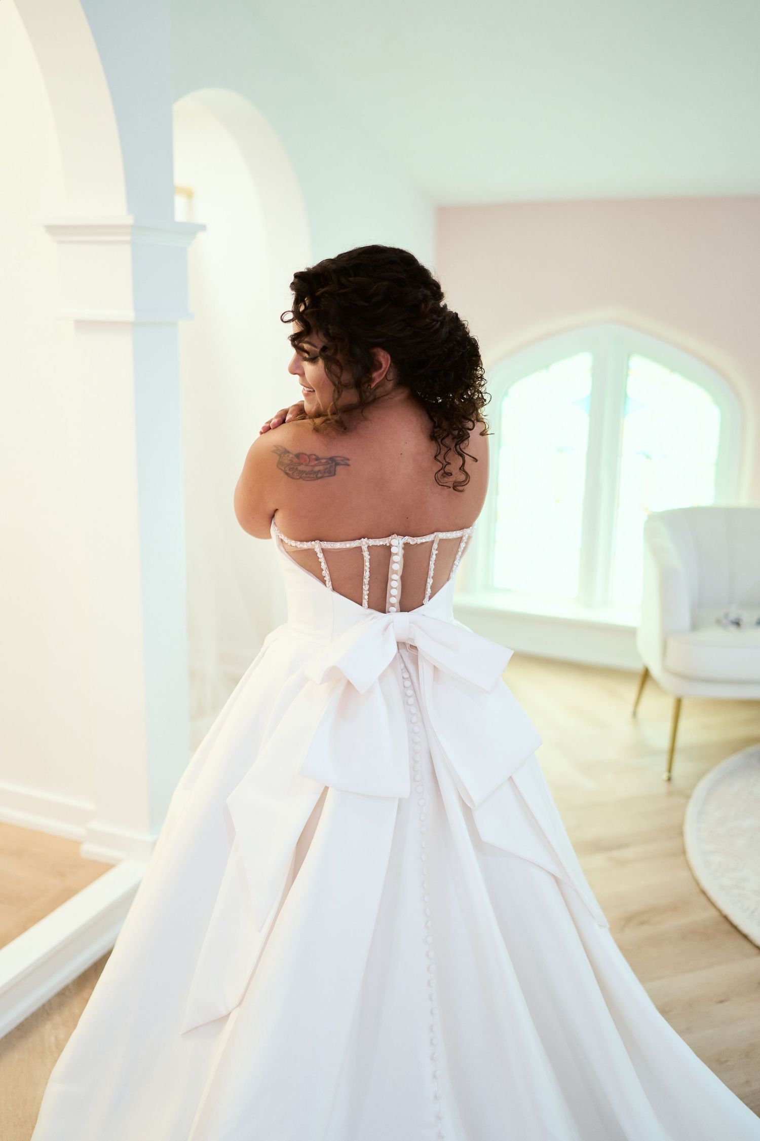 Back view of a white wedding gown with button details and large bow accent.