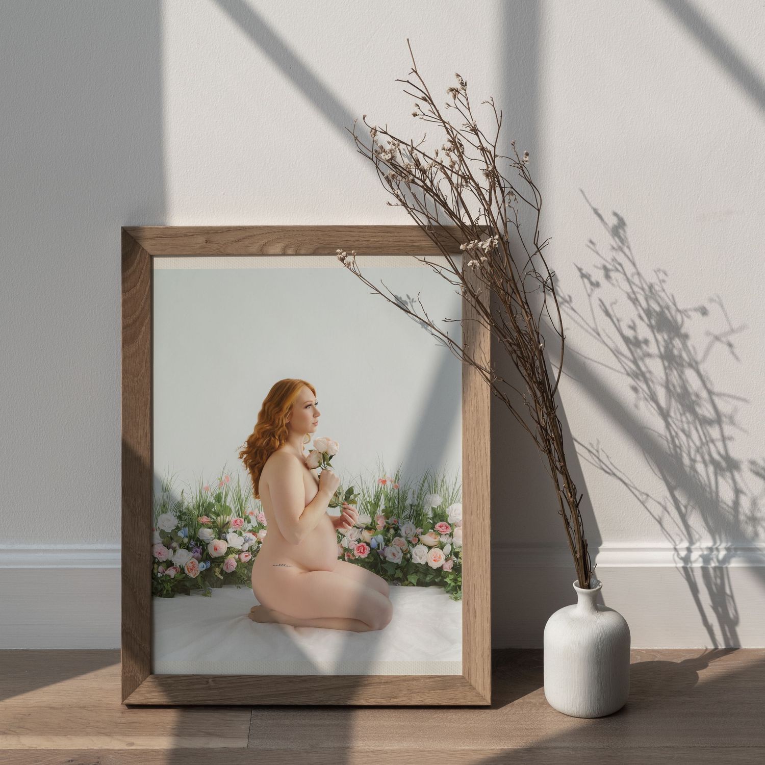 A framed maternity photo displayed with dried branches and a white vase against a light wall.