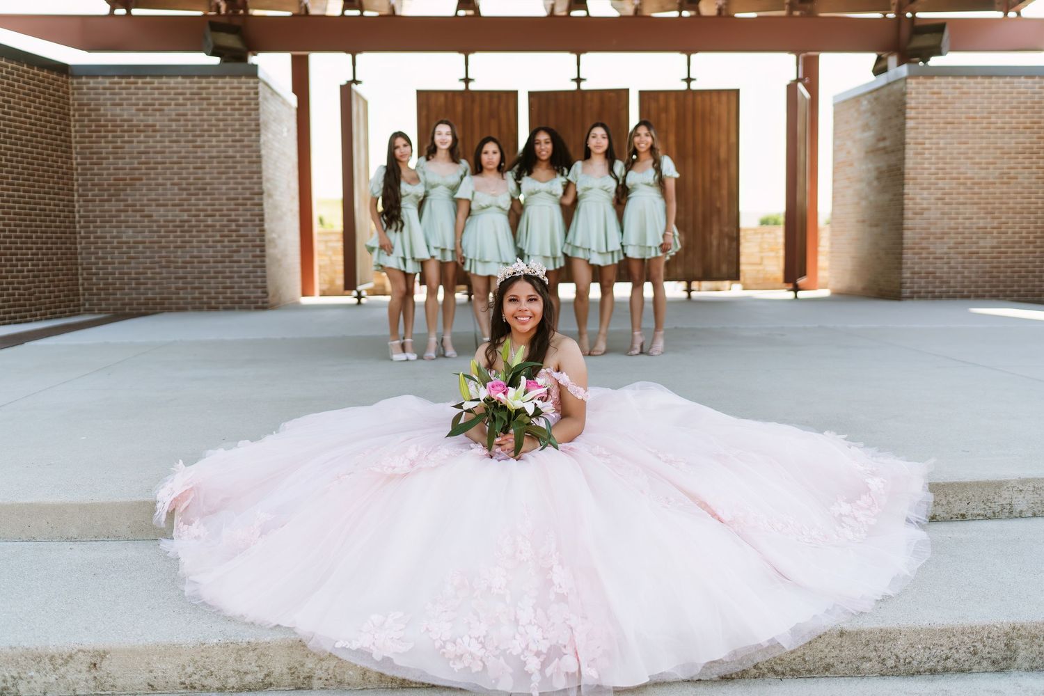 Wedding party members in coordinating pink dresses pose along a brick wall for a series of formal photos.
