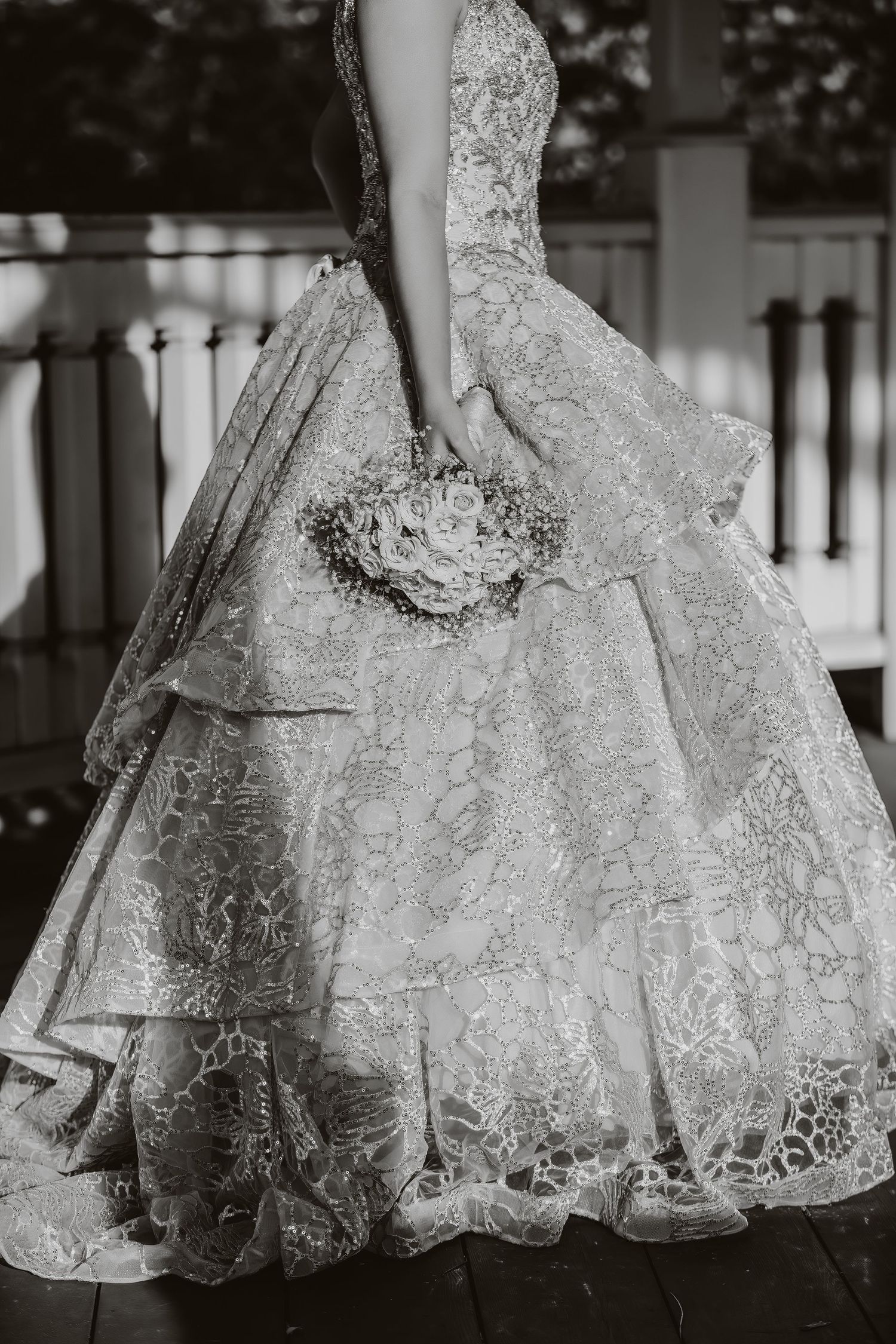 Close-up detail of an intricate lace wedding dress with layers and a bouquet.