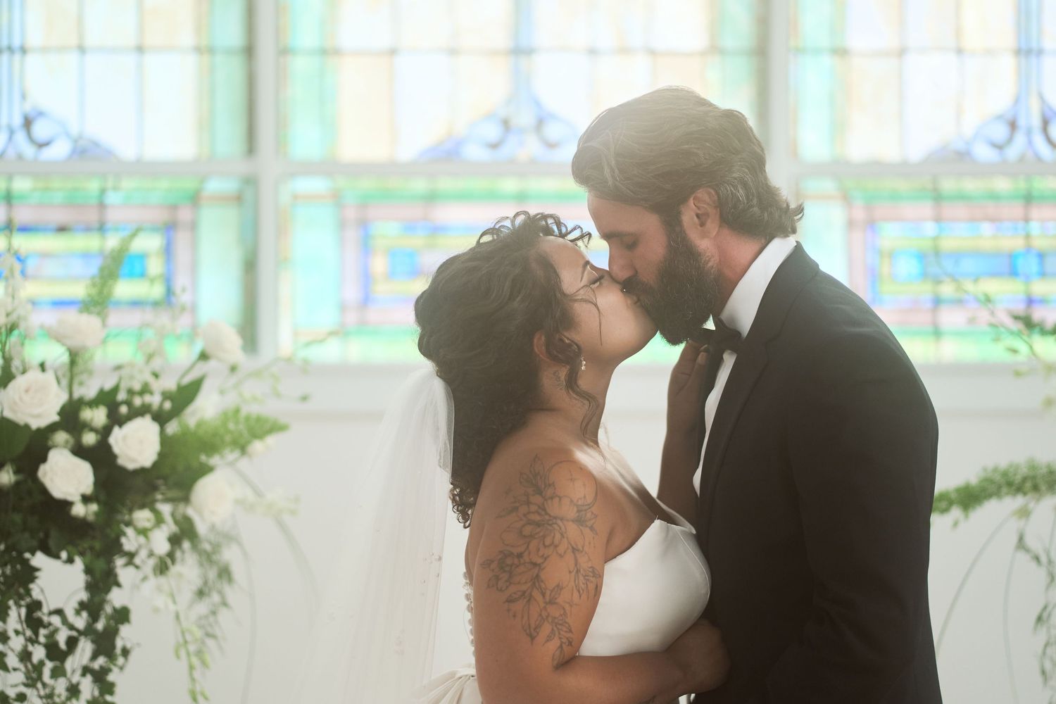Newlyweds share their first kiss as a married couple in a wedding ceremony with floral decorations.
