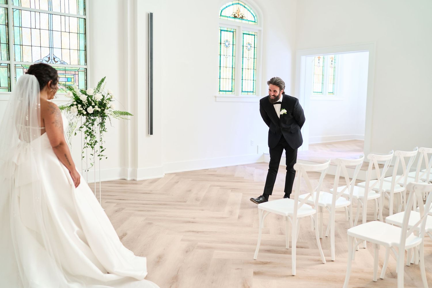 White wedding ceremony space with rows of chairs and stained glass windows letting in natural light.