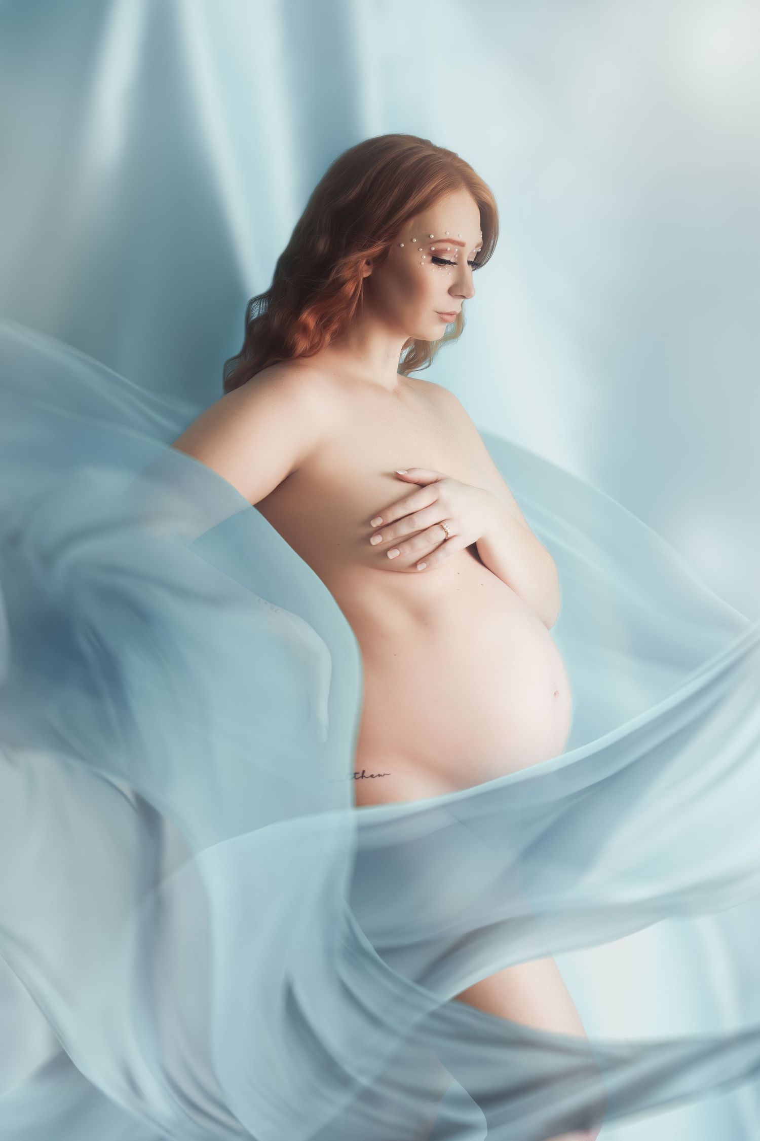 Ethereal maternity portrait with flowing blue fabric creating a dreamy atmosphere.