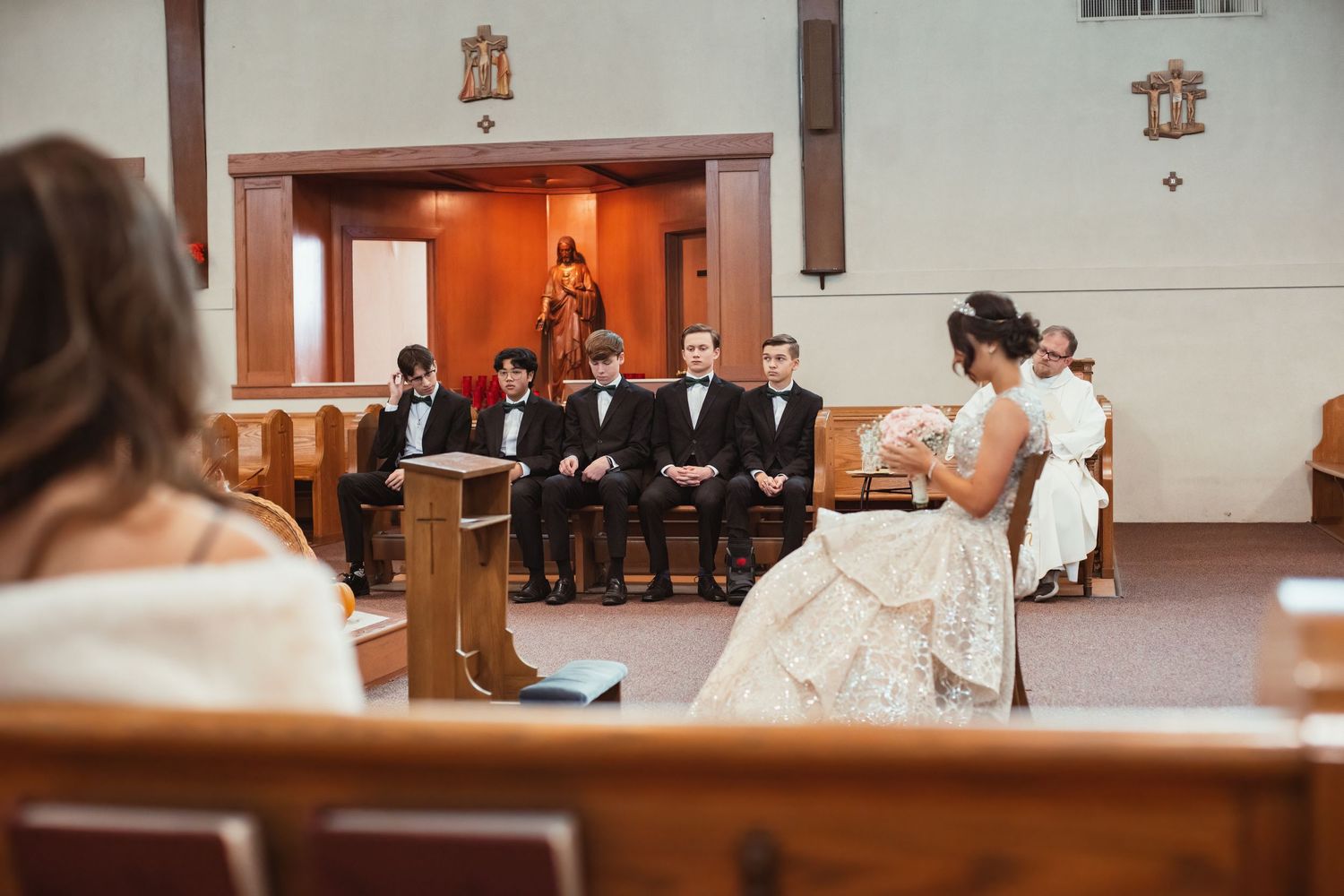 A wedding ceremony in progress inside a traditional Catholic church with wooden pews and decorative details.