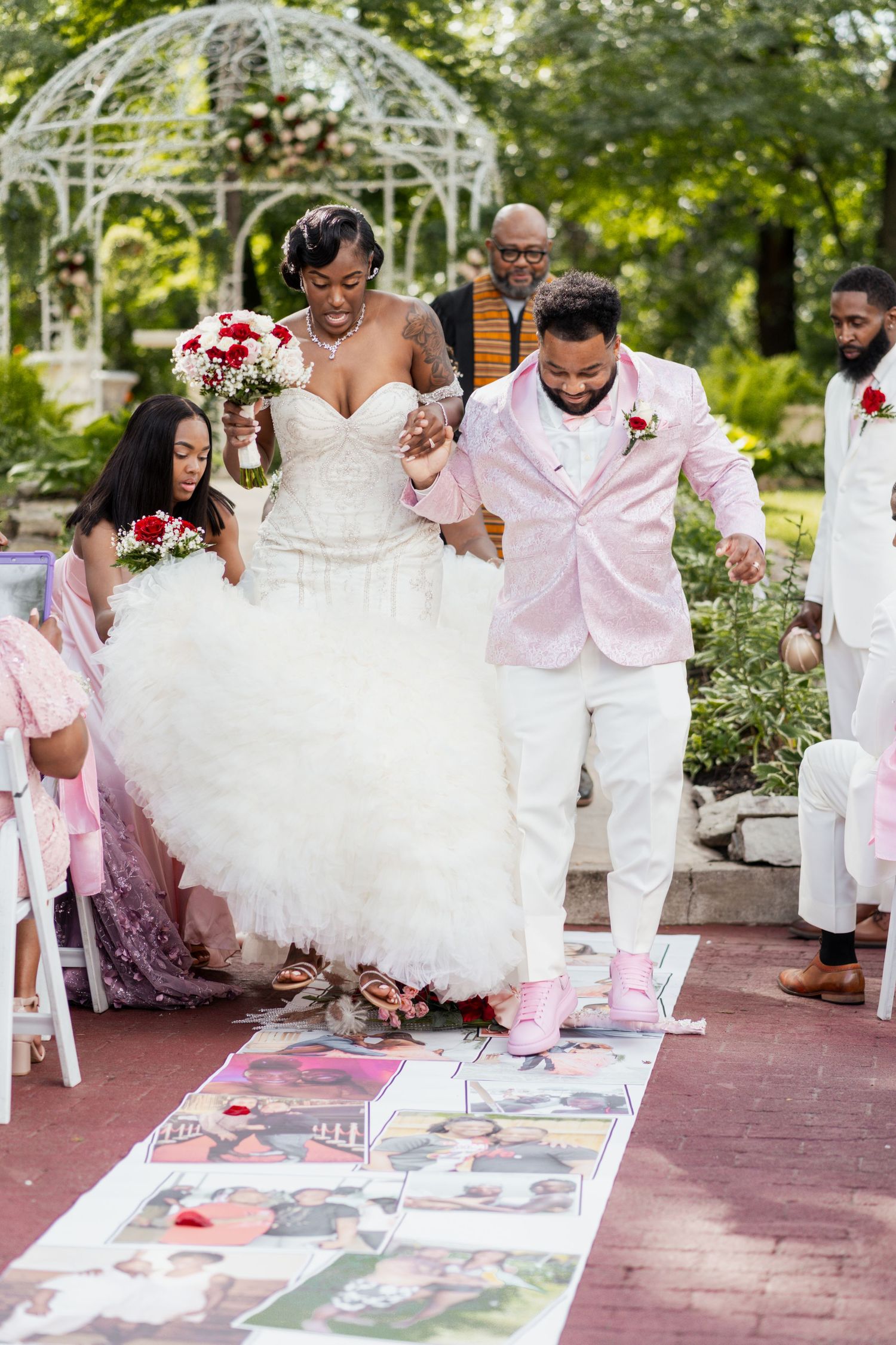 Couple walks across photo-lined aisle during outdoor wedding ceremony.