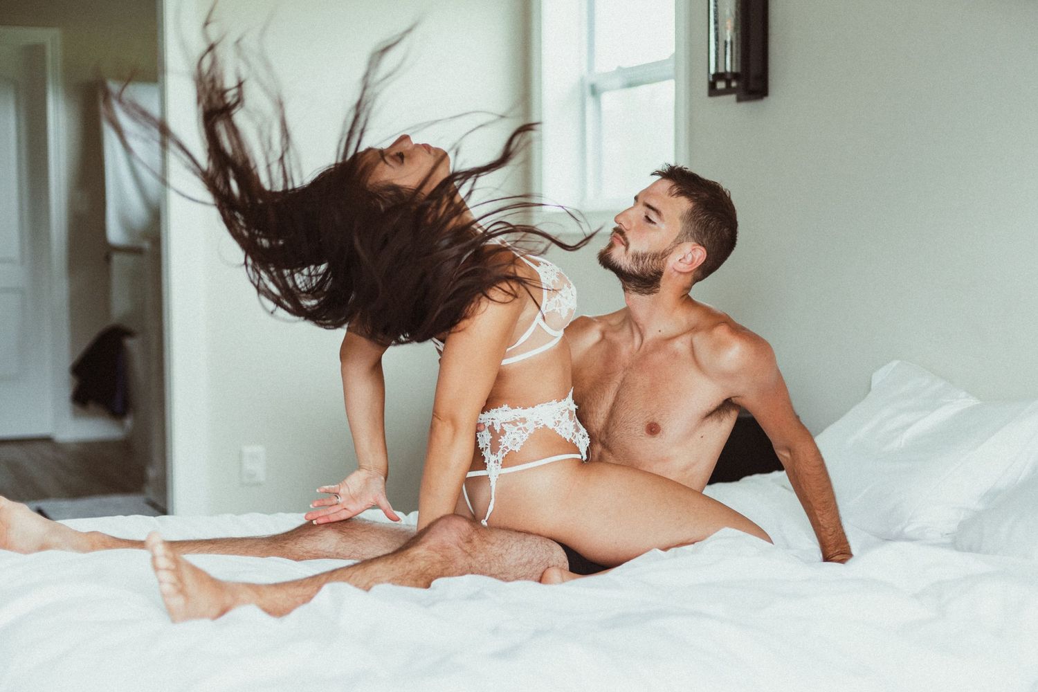 A couple in white lingerie sharing an intimate moment on white bedding.