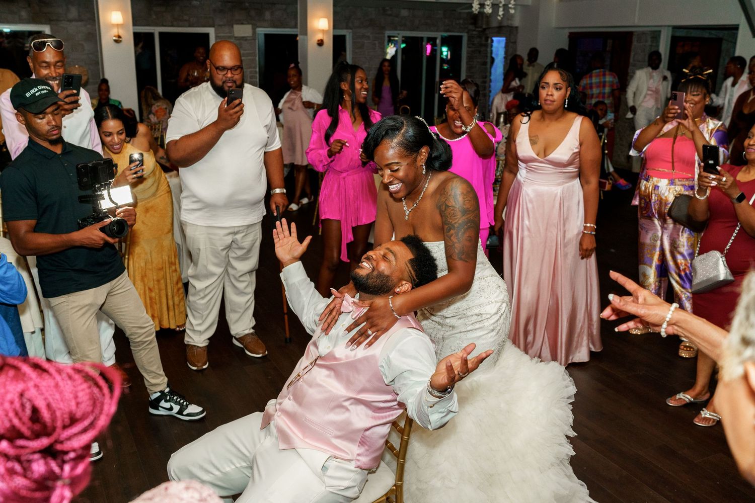 Energetic dance floor moment captured during wedding reception celebration with guests in pink attire.