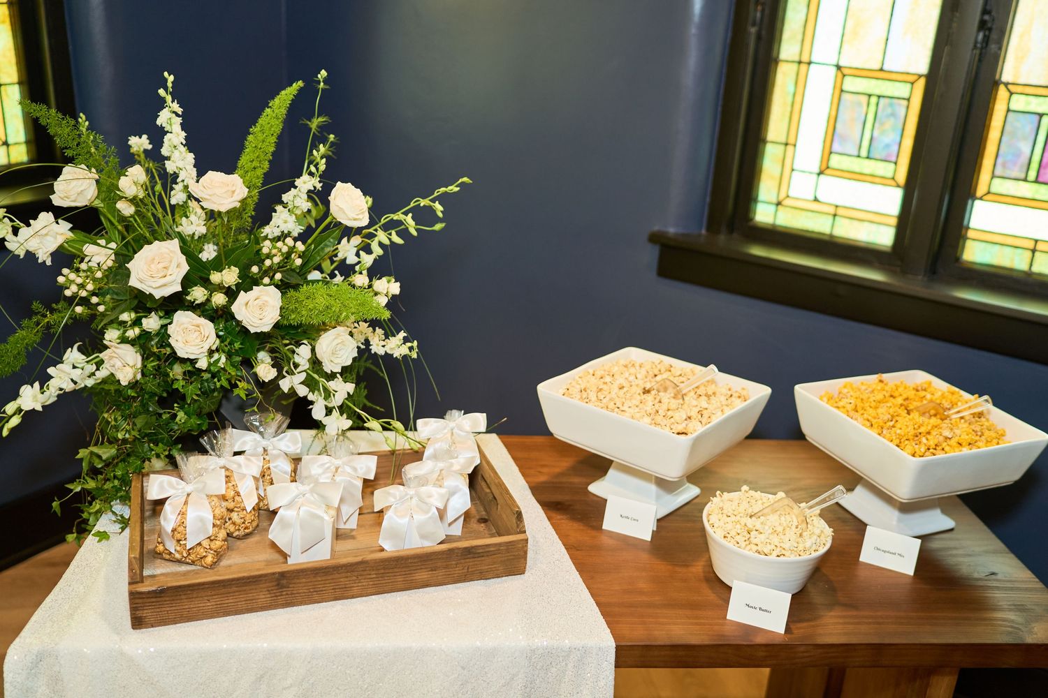 A wedding reception snack table with elegant floral arrangements and white serving dishes filled with treats.