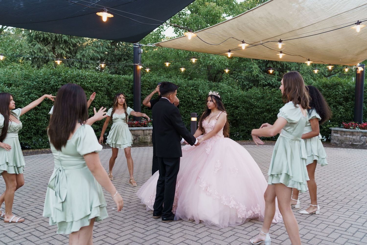 Wedding party members in light mint green dresses gather on a paved outdoor patio area.