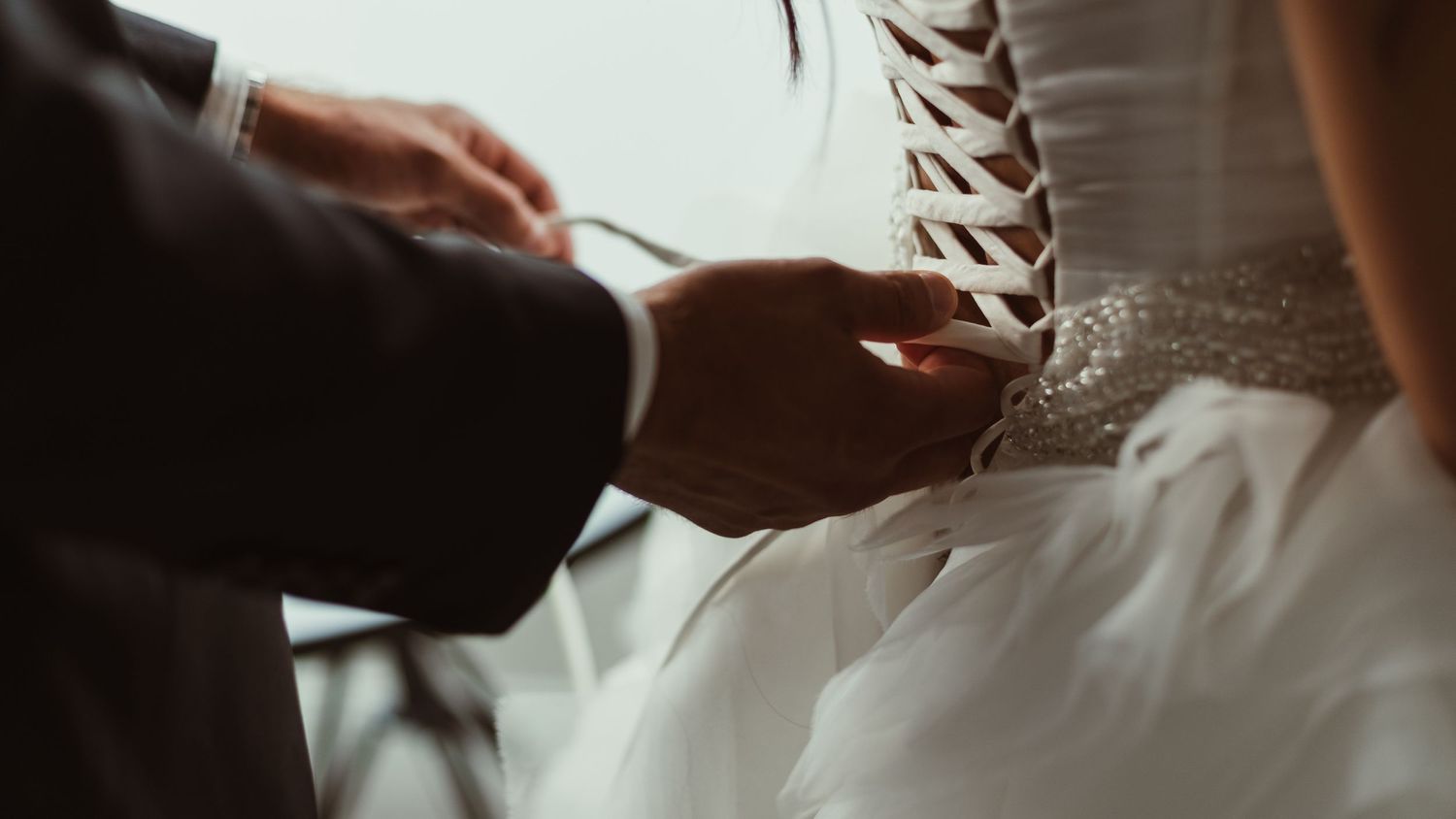 Close-up of fingers carefully threading wedding dress corset.