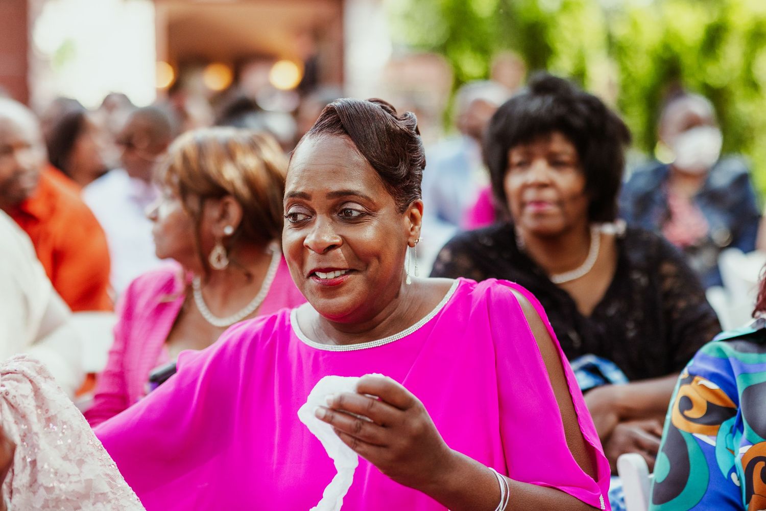 Guest in bright pink outfit enjoys festive moment during outdoor wedding celebration.