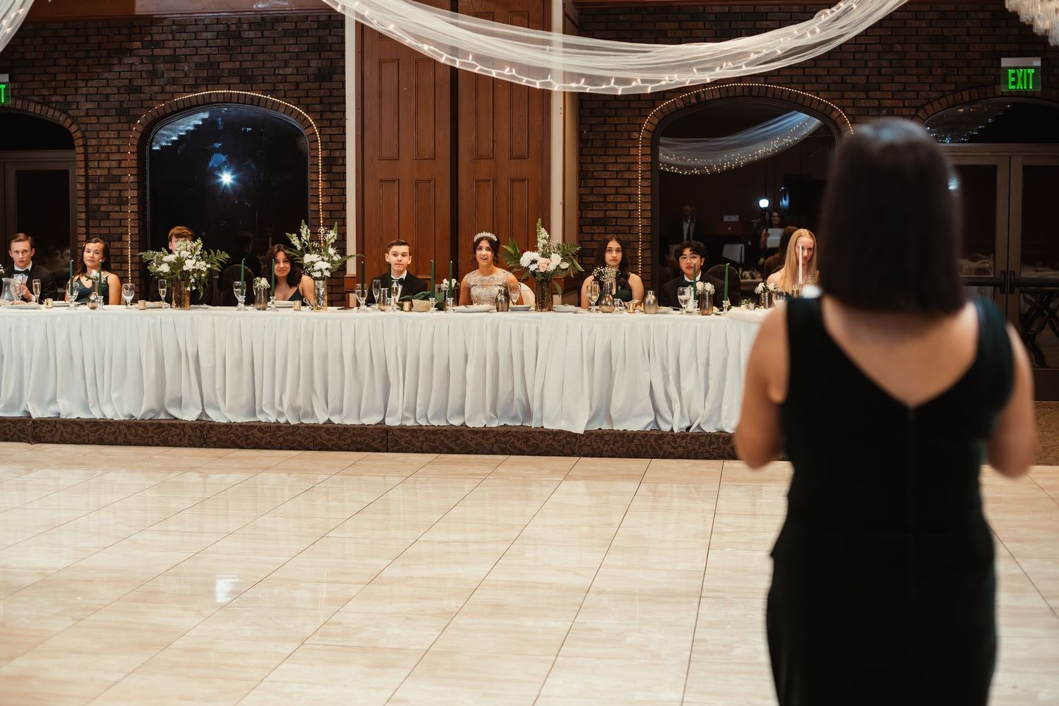 A view of the head table at a wedding reception with elegant white decor and brick archways.
