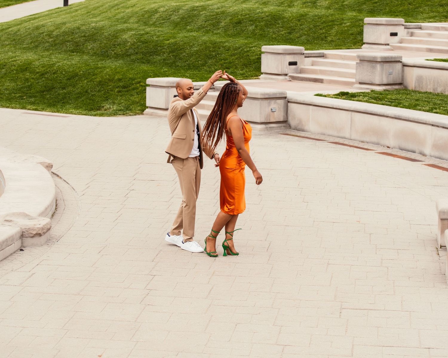 Dancing couple twirling on stone steps wearing orange dress and beige suit.