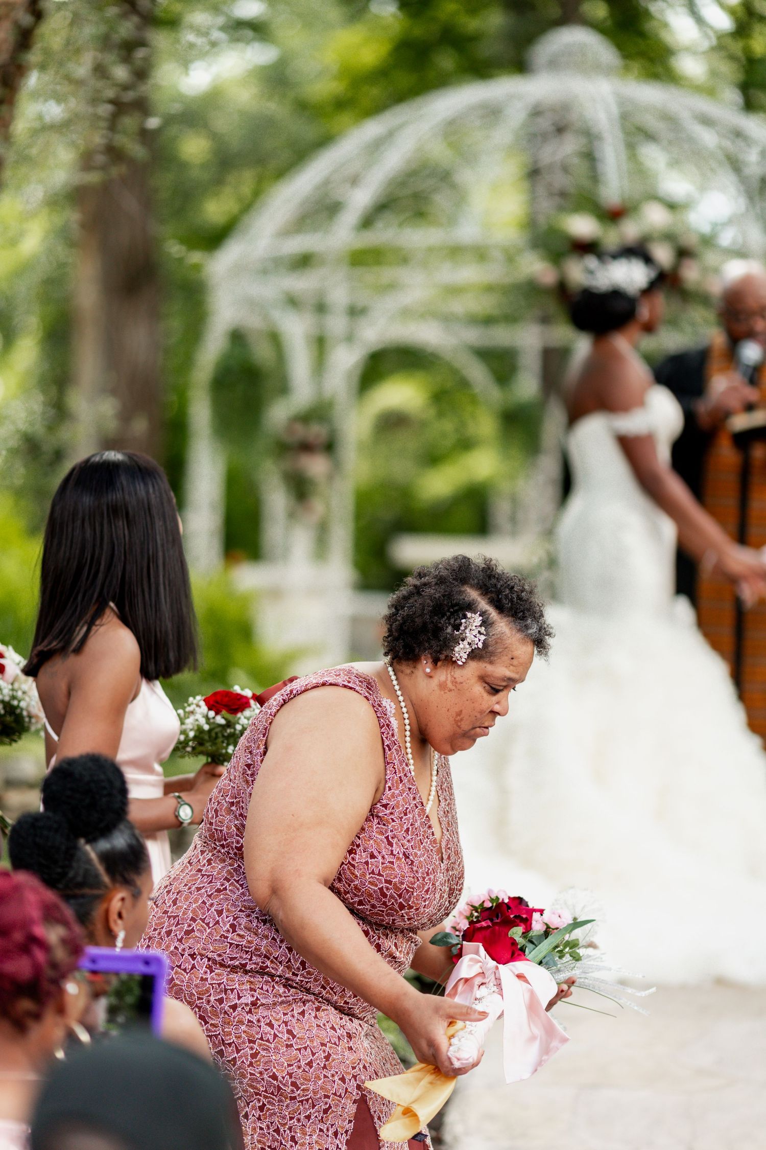Wedding guest in pink dress arranges items during outdoor ceremony.
