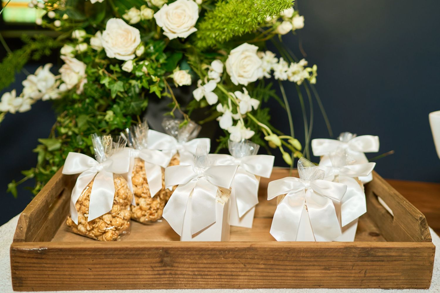 White gift boxes with bows arranged in wooden tray with floral decorations.
